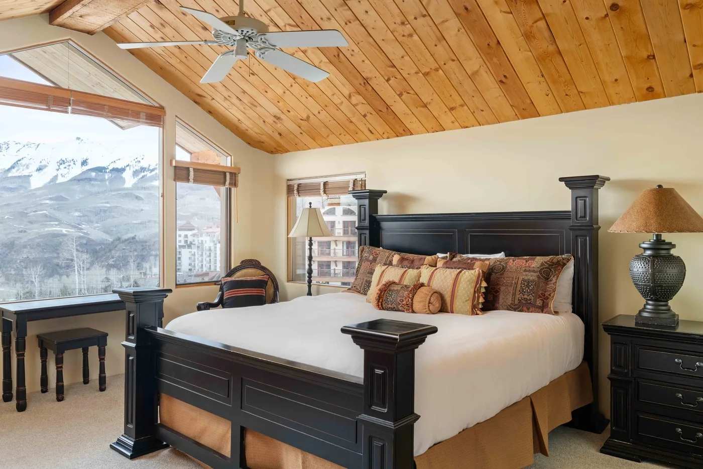 Un dormitorio con una cama grande, techo revestido de madera y vistas a las montañas por las ventanas.
