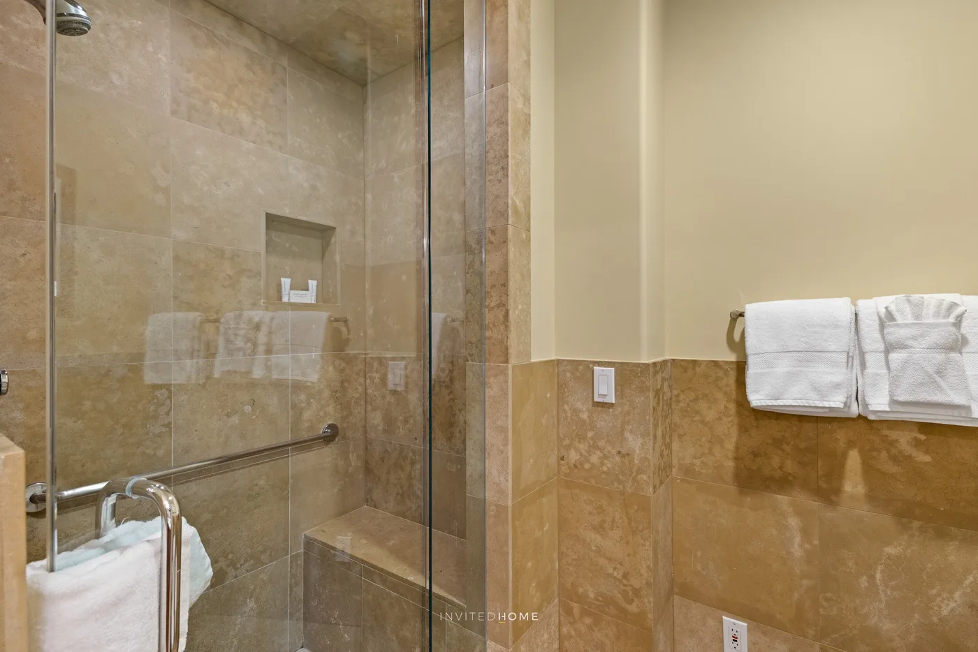Un baño alicatado con una ducha de vidrio y toallas dobladas en un toallero.