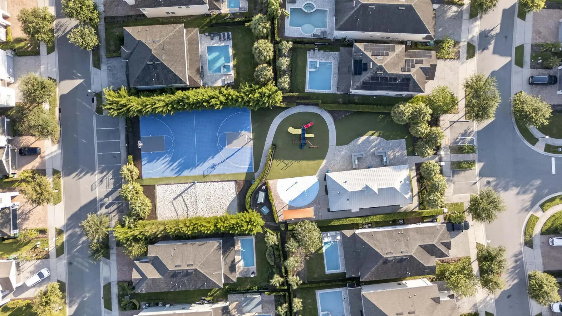 An aerial view of a residential neighborhood with houses, pools, and a sports court.