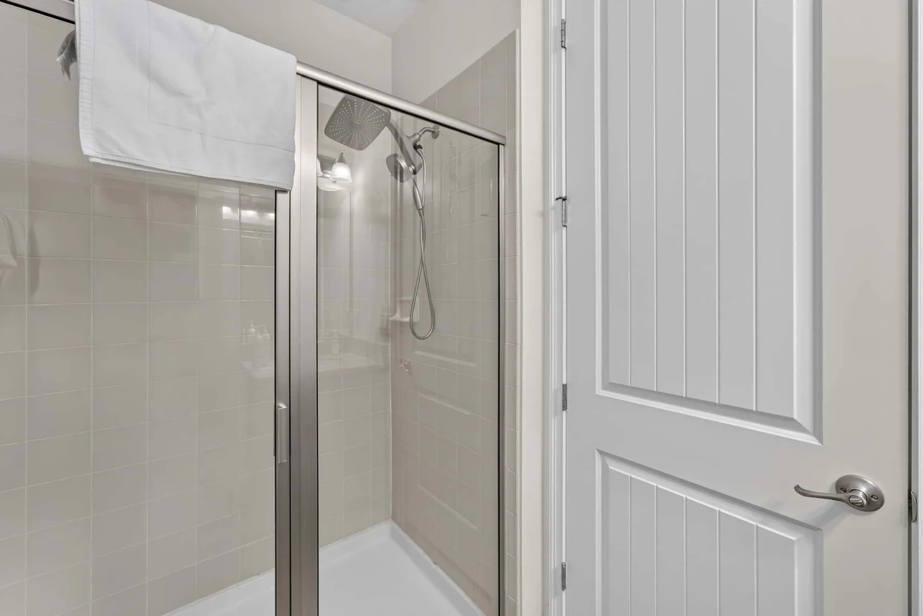 A bathroom with a glass shower and a paneled door.
