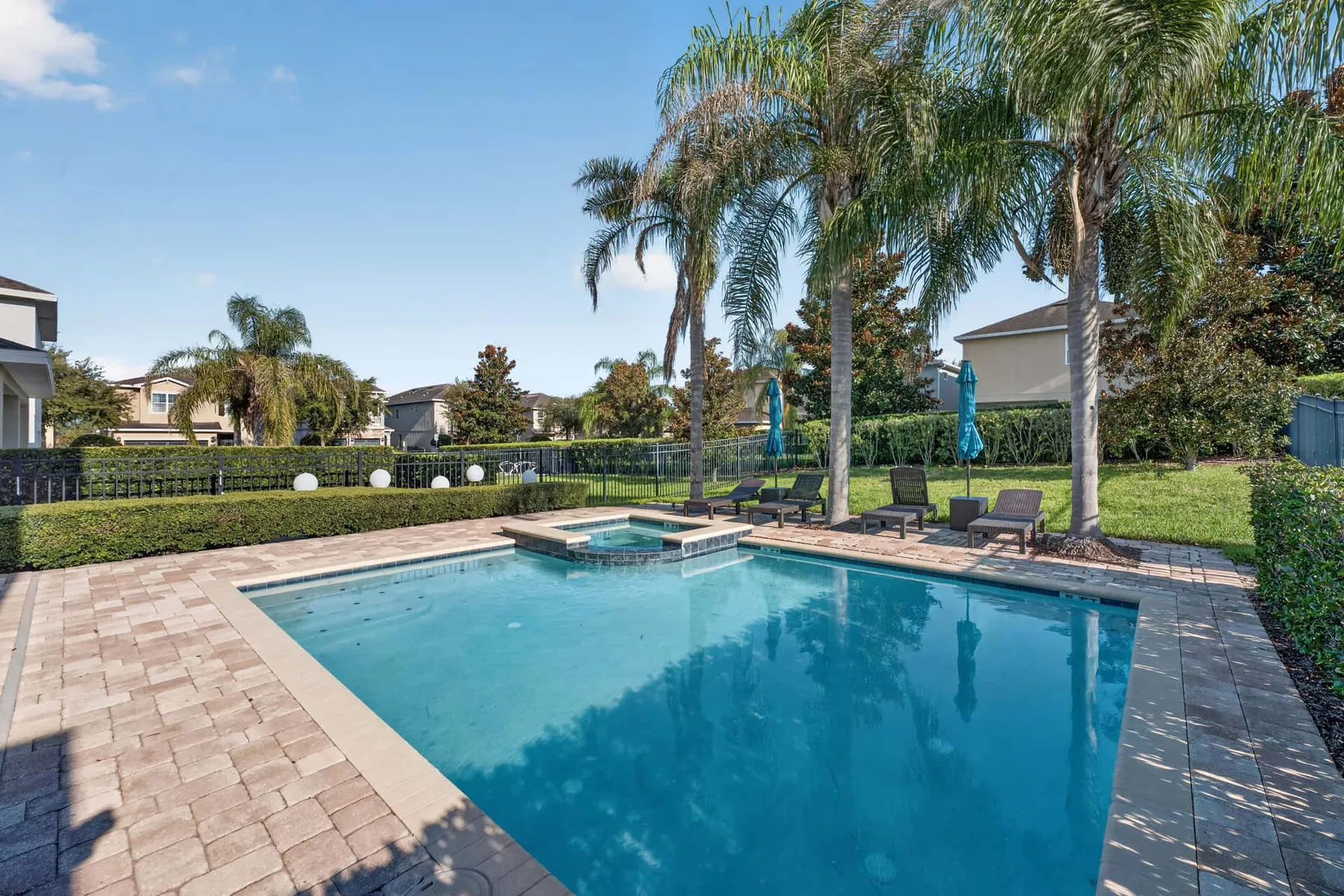 An outdoor swimming pool with a raised spa, surrounded by paved decking and palm trees.