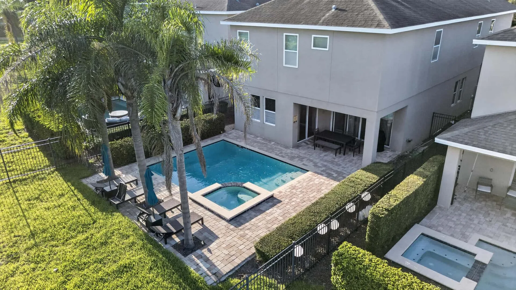 Aerial view of a swimming pool and patio beside a modern house.