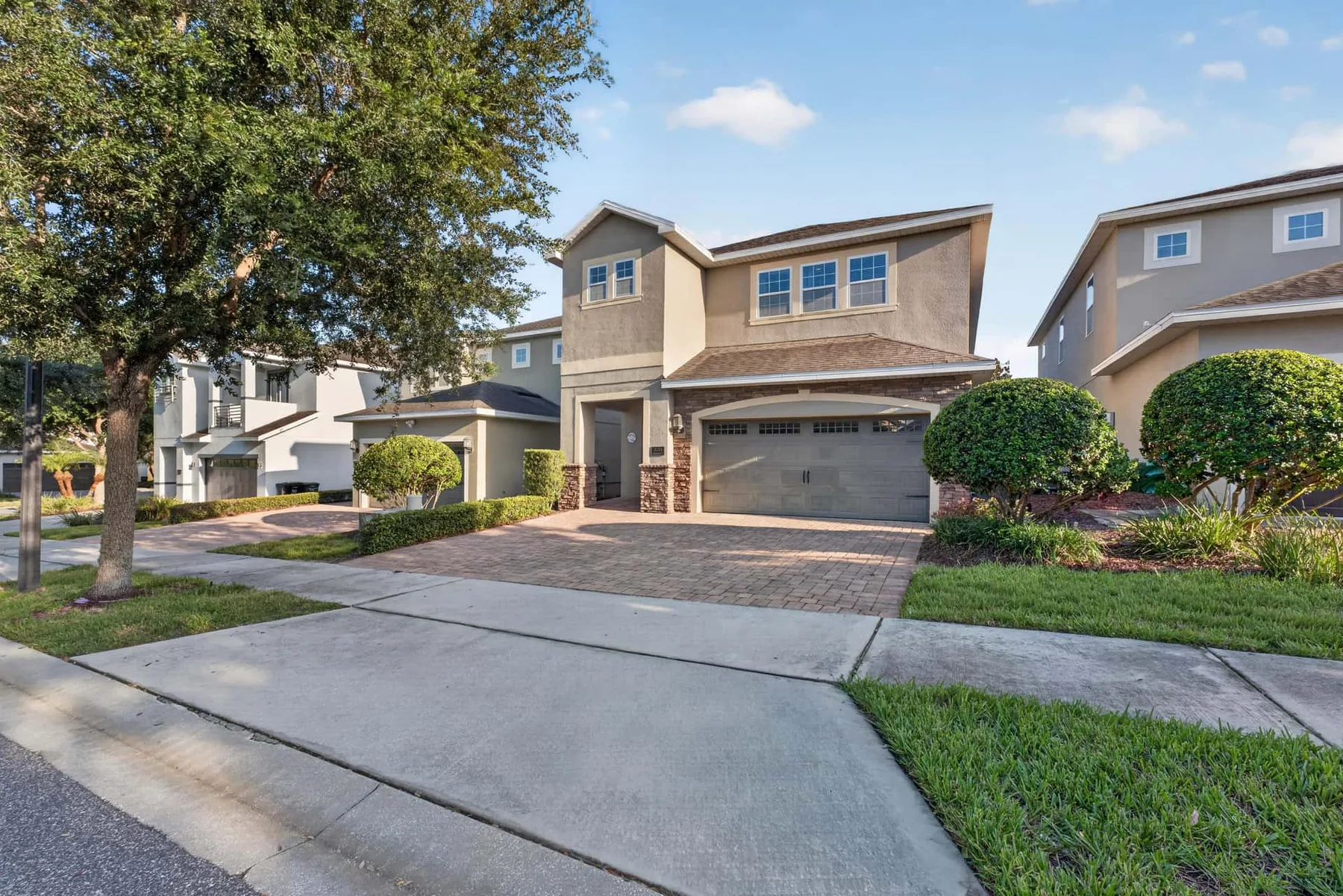 A suburban residential street with two-story houses, driveways, and front lawns.
