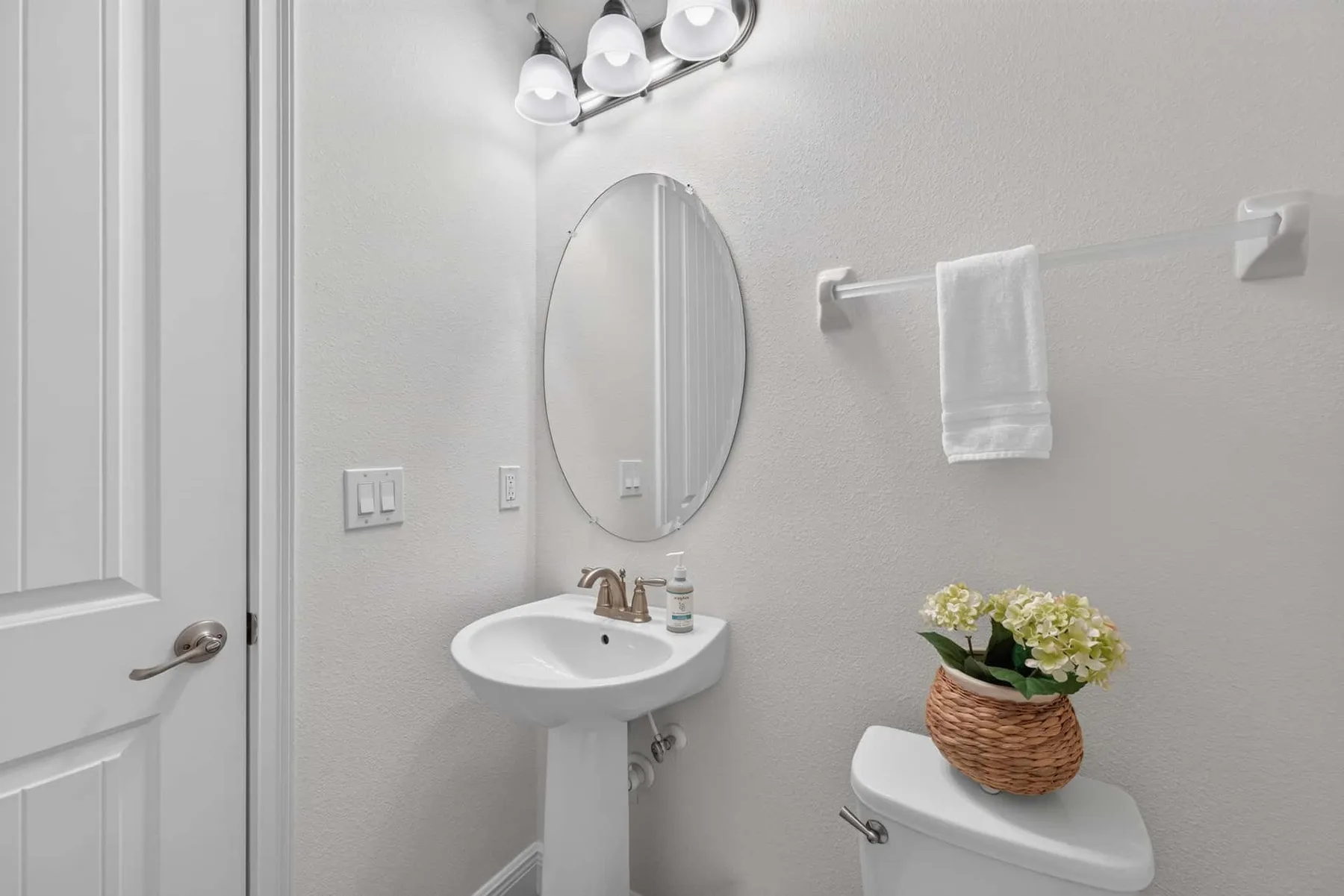 A bathroom with a sink, oval mirror, and towel hanging on the wall.