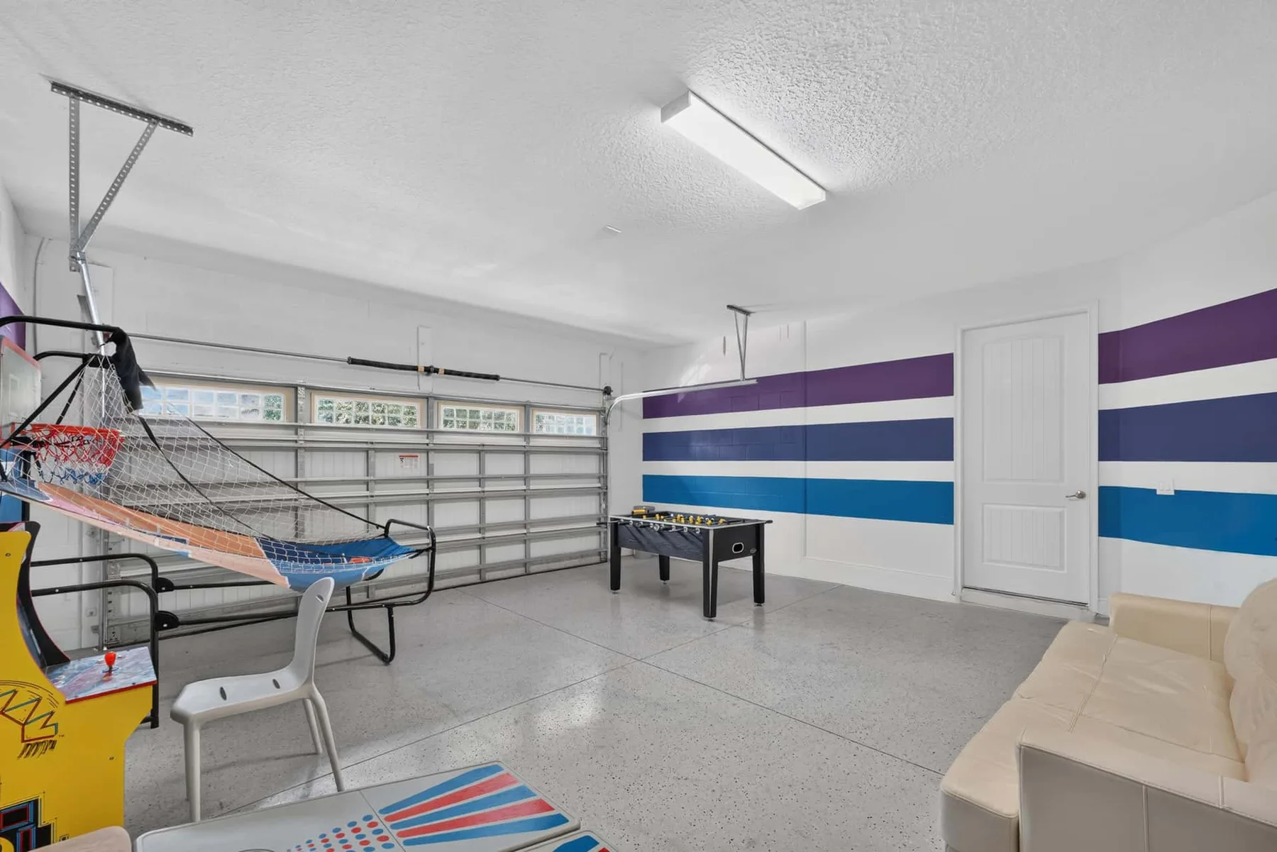 A garage recreation room has a ping-pong table, seating, and a basketball game.