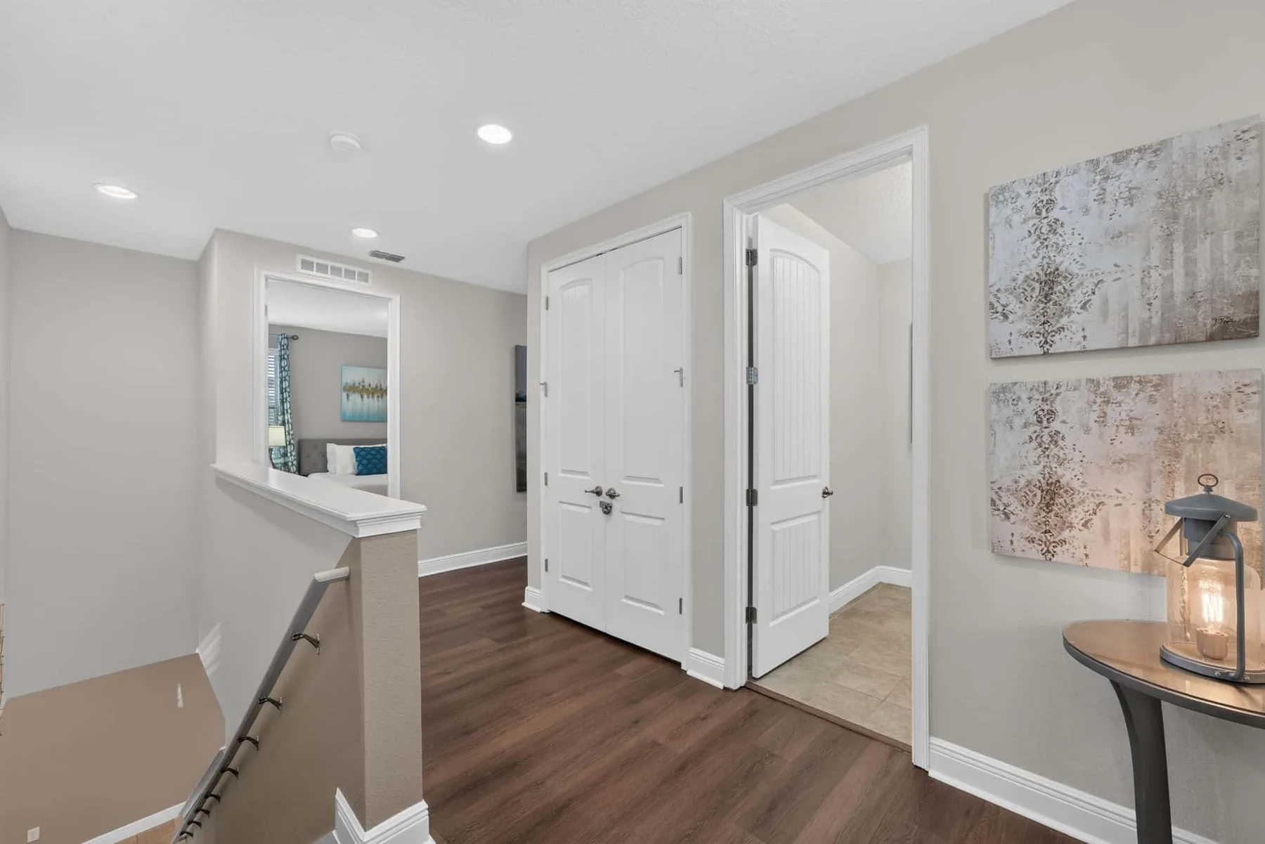 A bright hallway with white doors, wood flooring, and wall art.