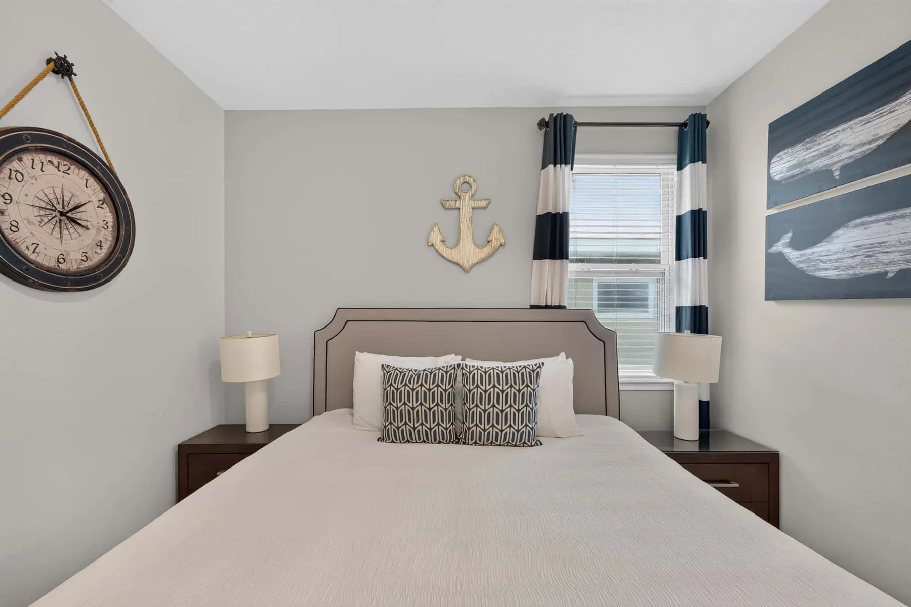 A bedroom with a neatly made bed, bedside tables, and nautical wall decorations.