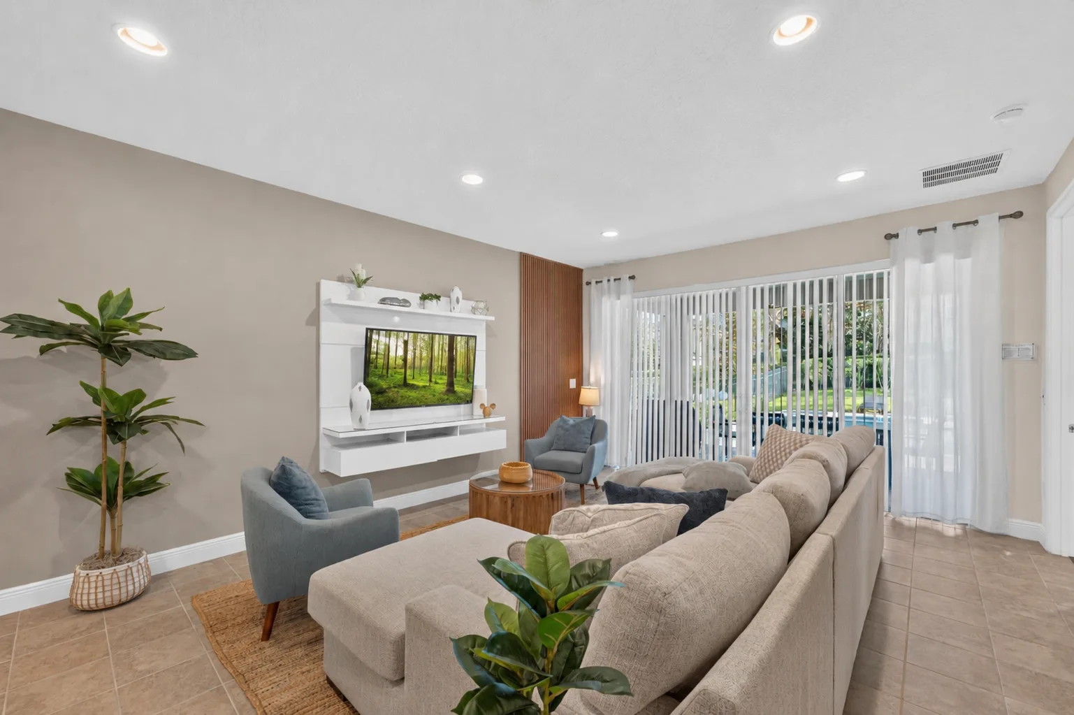 A bright living room with seating arranged around a television and large windows.