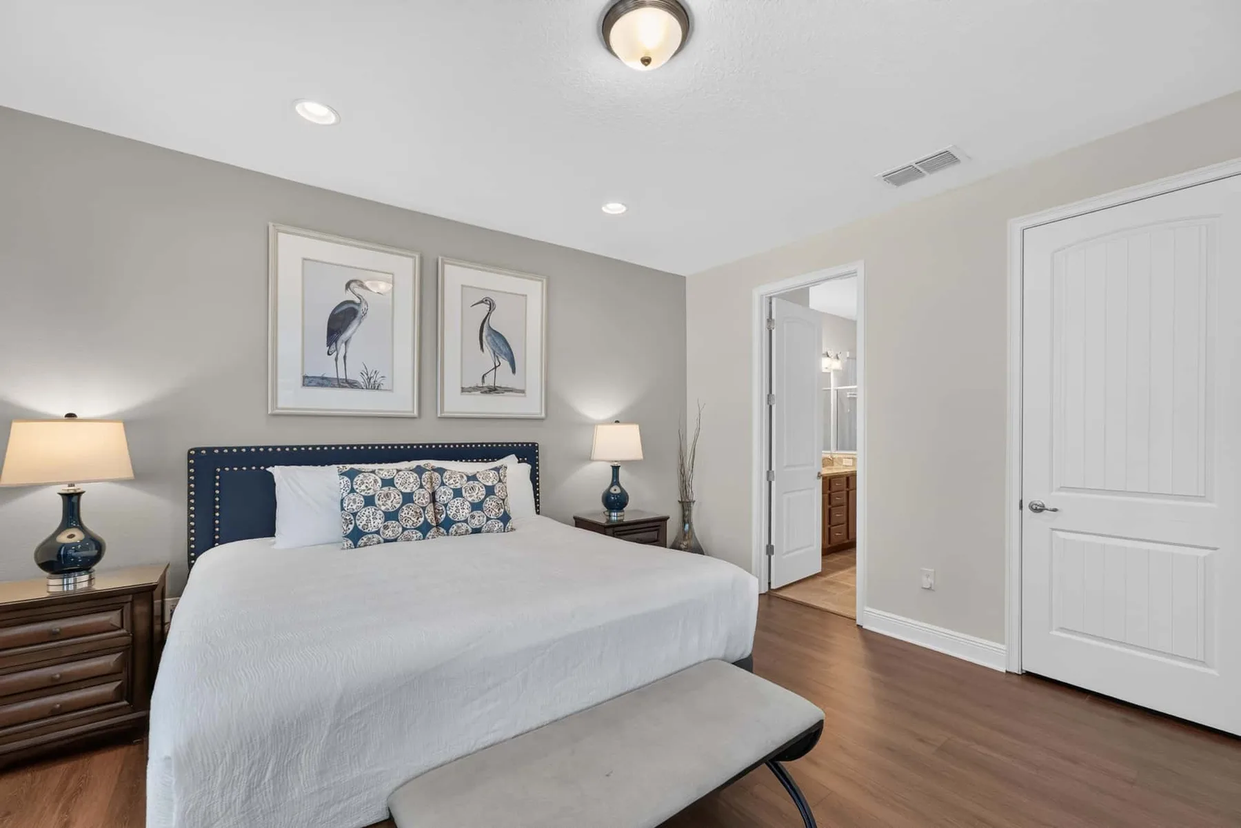 A bedroom with a neatly made bed beneath two framed bird prints.