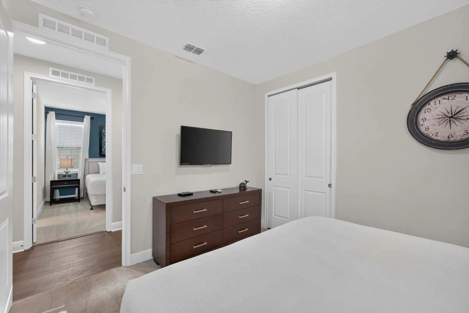 A bedroom with a bed, dresser, wall-mounted television, and closed closet doors.