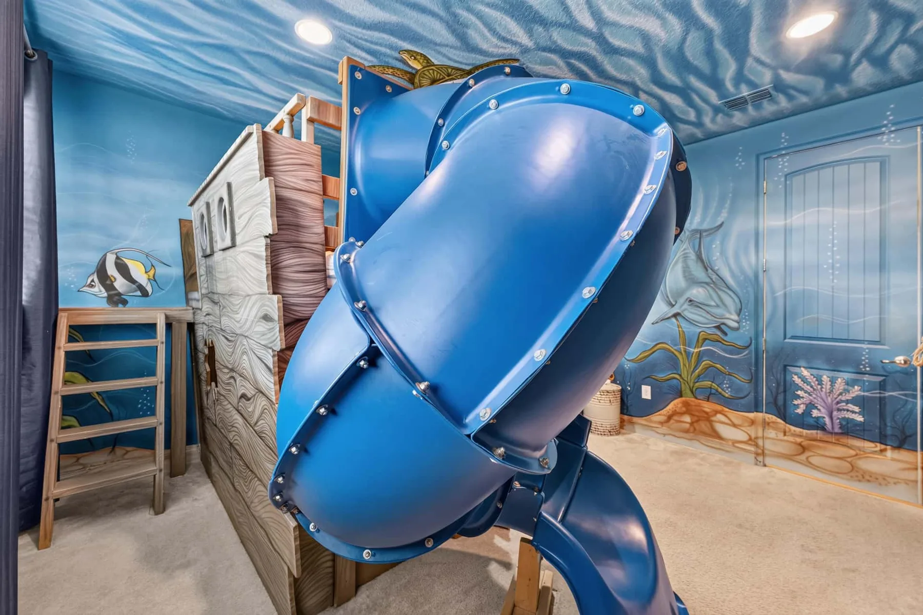 A brightly decorated playroom features a large blue indoor slide.