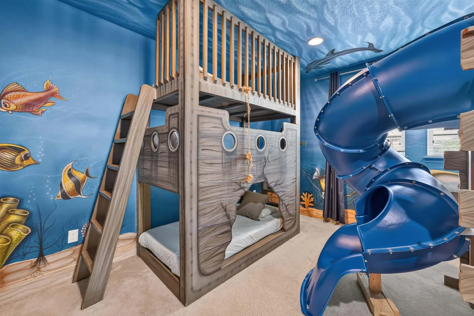 A themed children’s bedroom has a wooden bunk bed and a large blue slide.