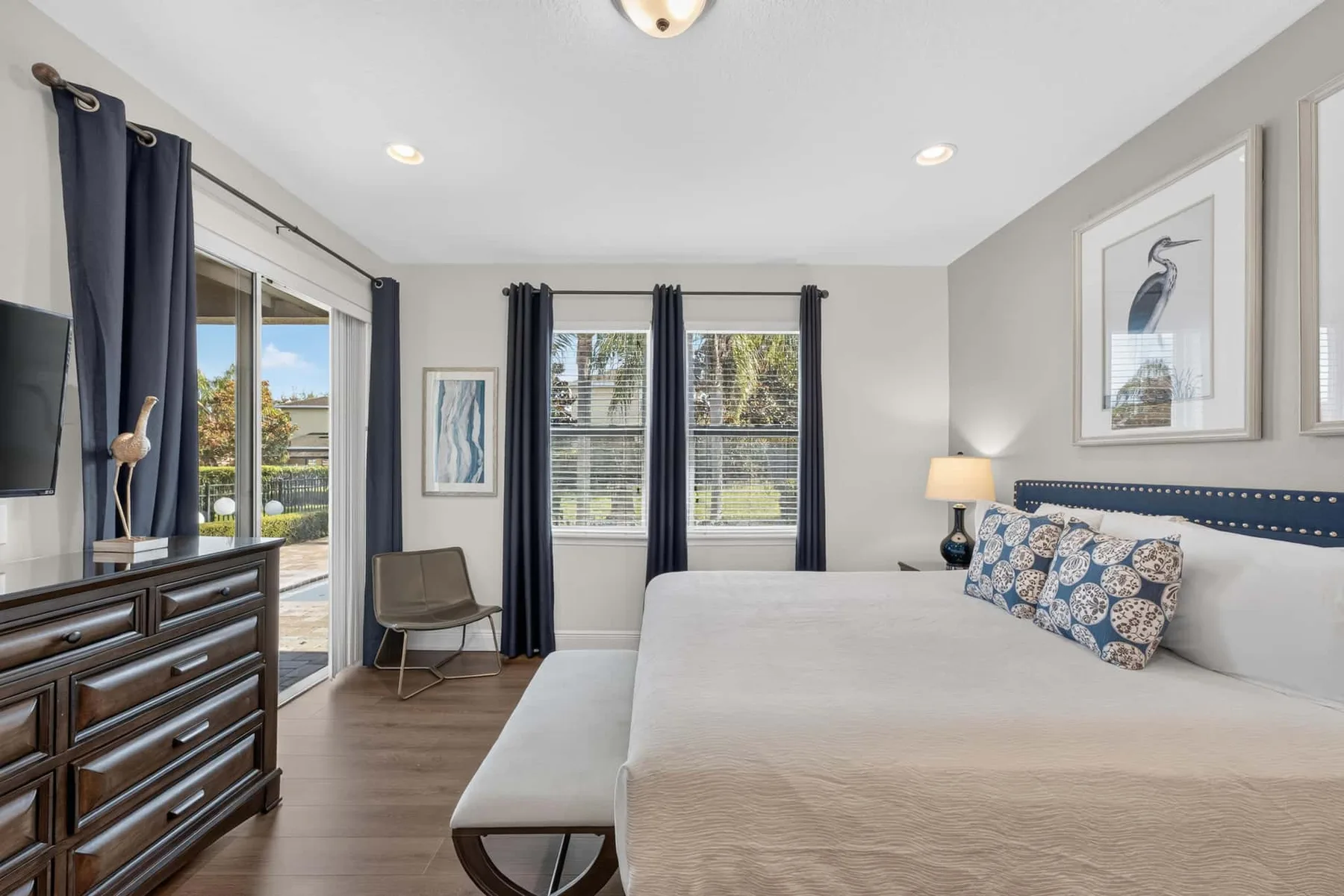 A bright bedroom with a bed, windows, and dark curtains.