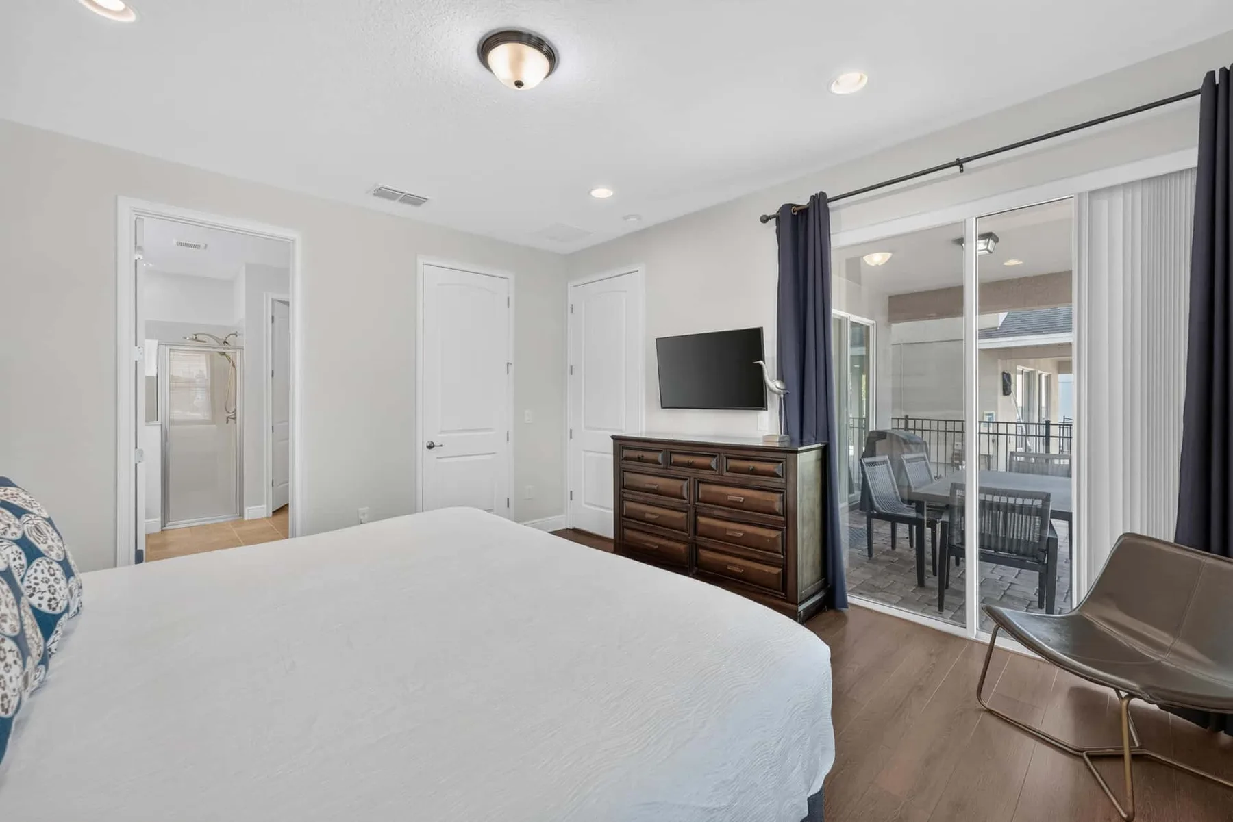 A bright bedroom with a bed, dresser, and sliding glass doors opening onto a patio.