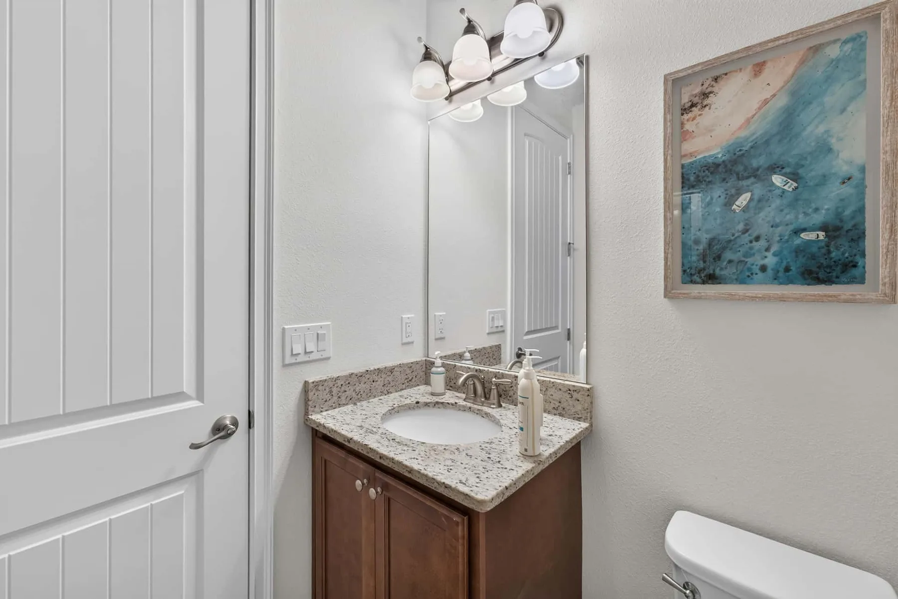 A bathroom vanity with a speckled countertop sits beneath a large mirror.