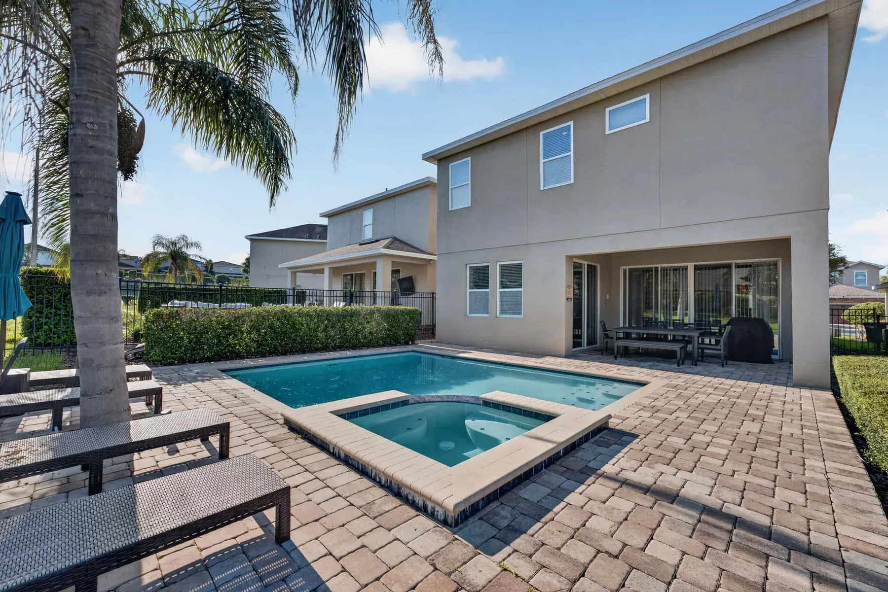A paved patio with a swimming pool sits beside a two-story house.
