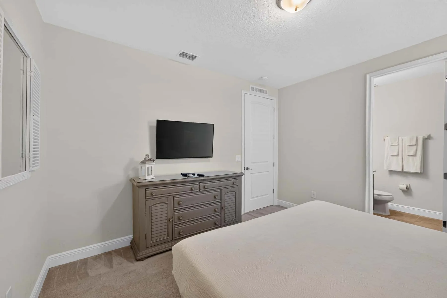 A bedroom with a bed, dresser, and wall-mounted television.