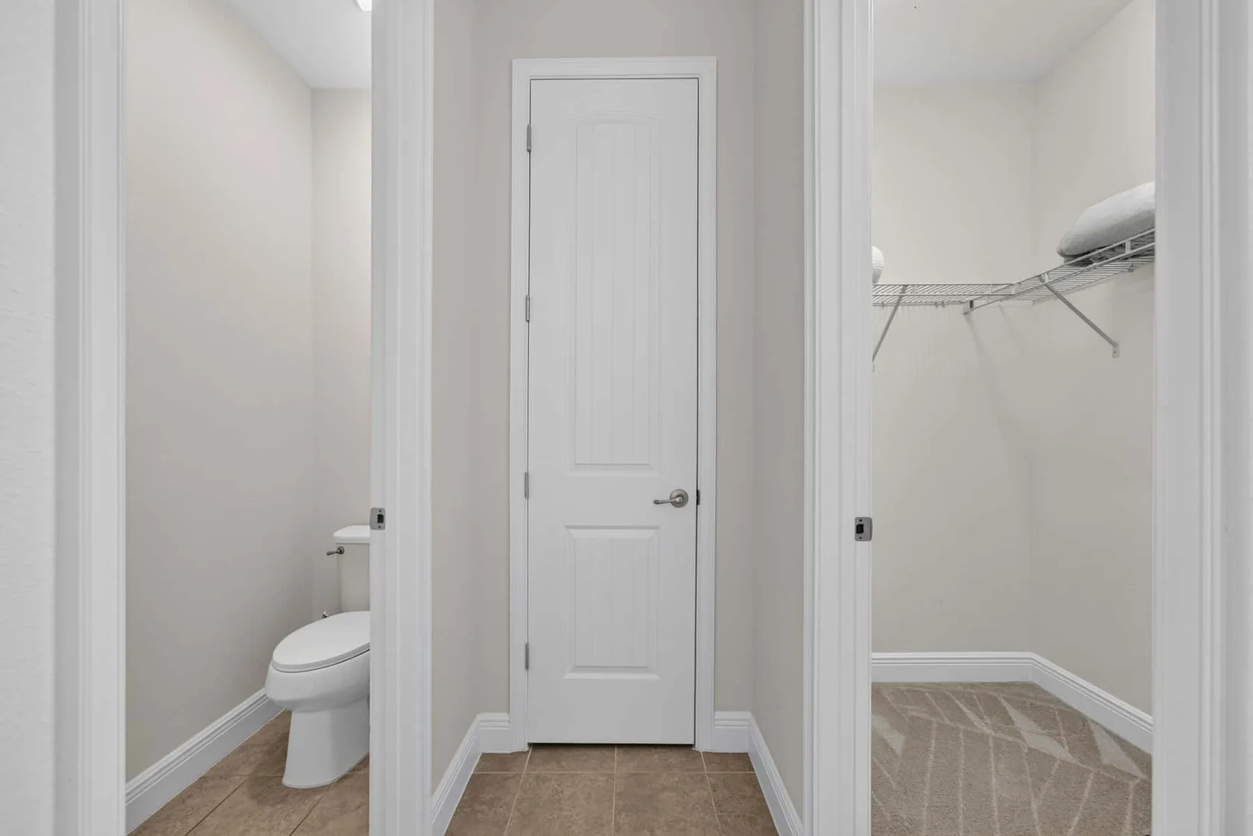A hallway with a closed door between a bathroom and an open closet.