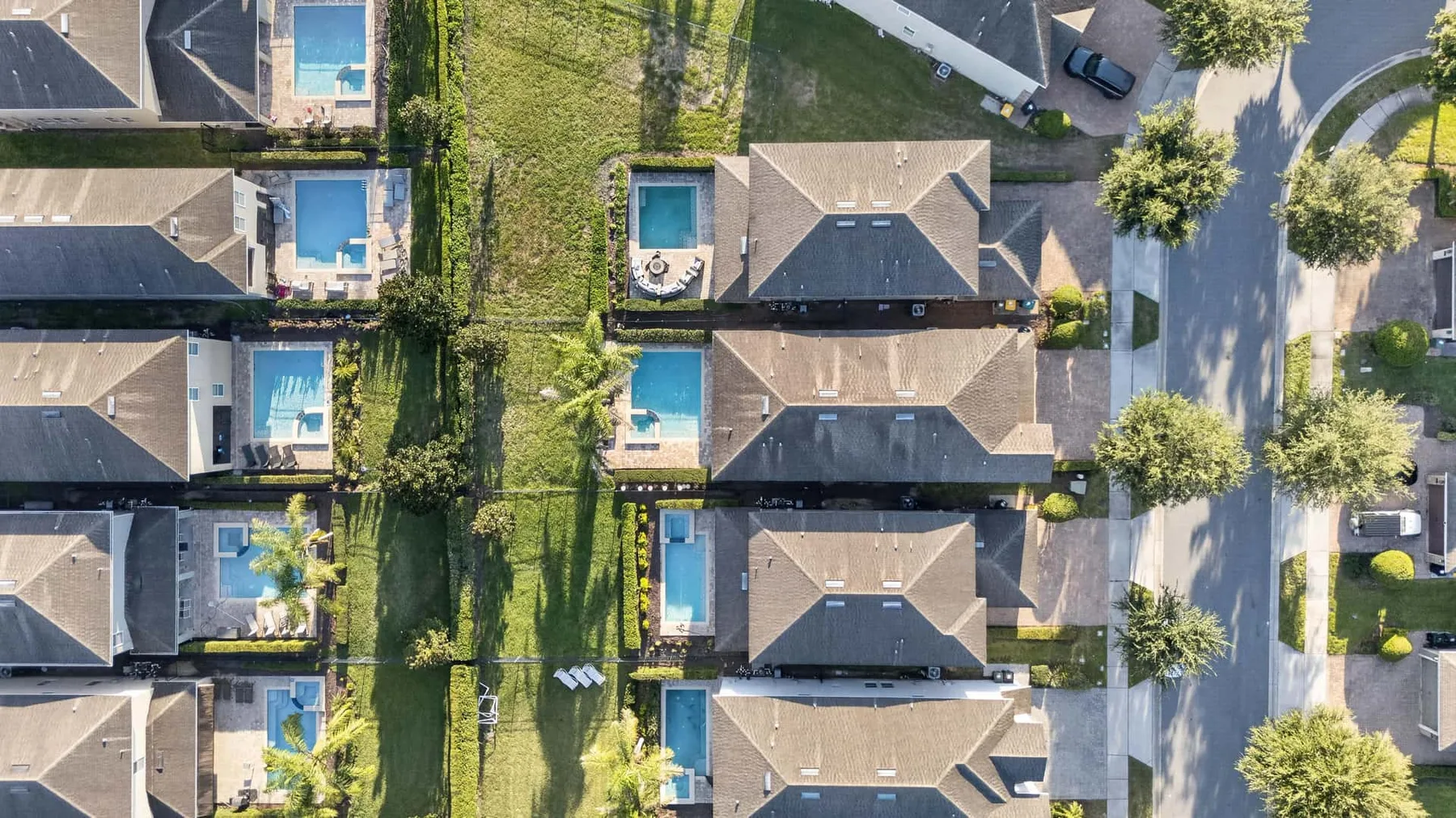 Aerial view of homes with swimming pools along a landscaped residential street.