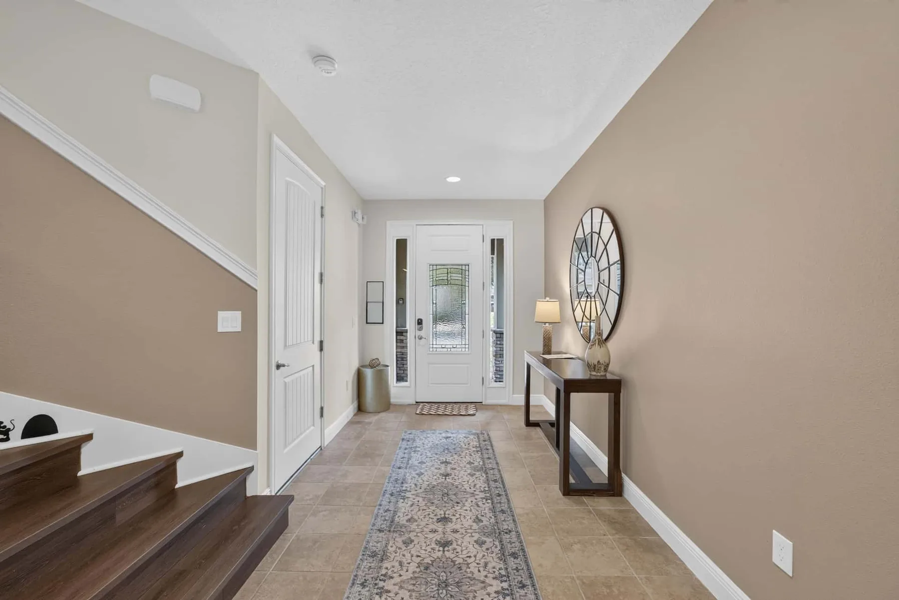 A tiled entry hall leads to a white front door, with a runner on the floor.
