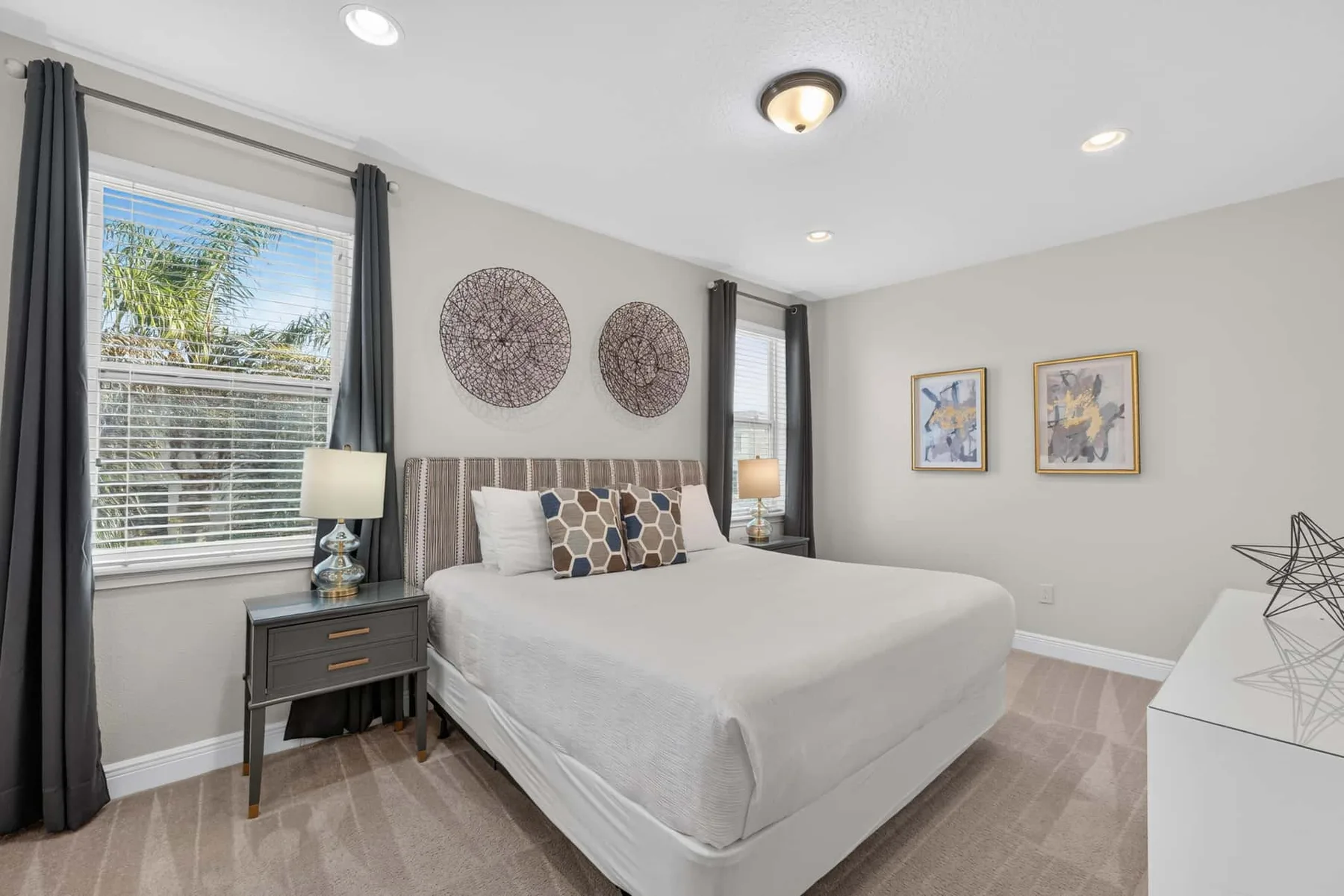 A bedroom with a neatly made bed, bedside tables, and framed wall art.