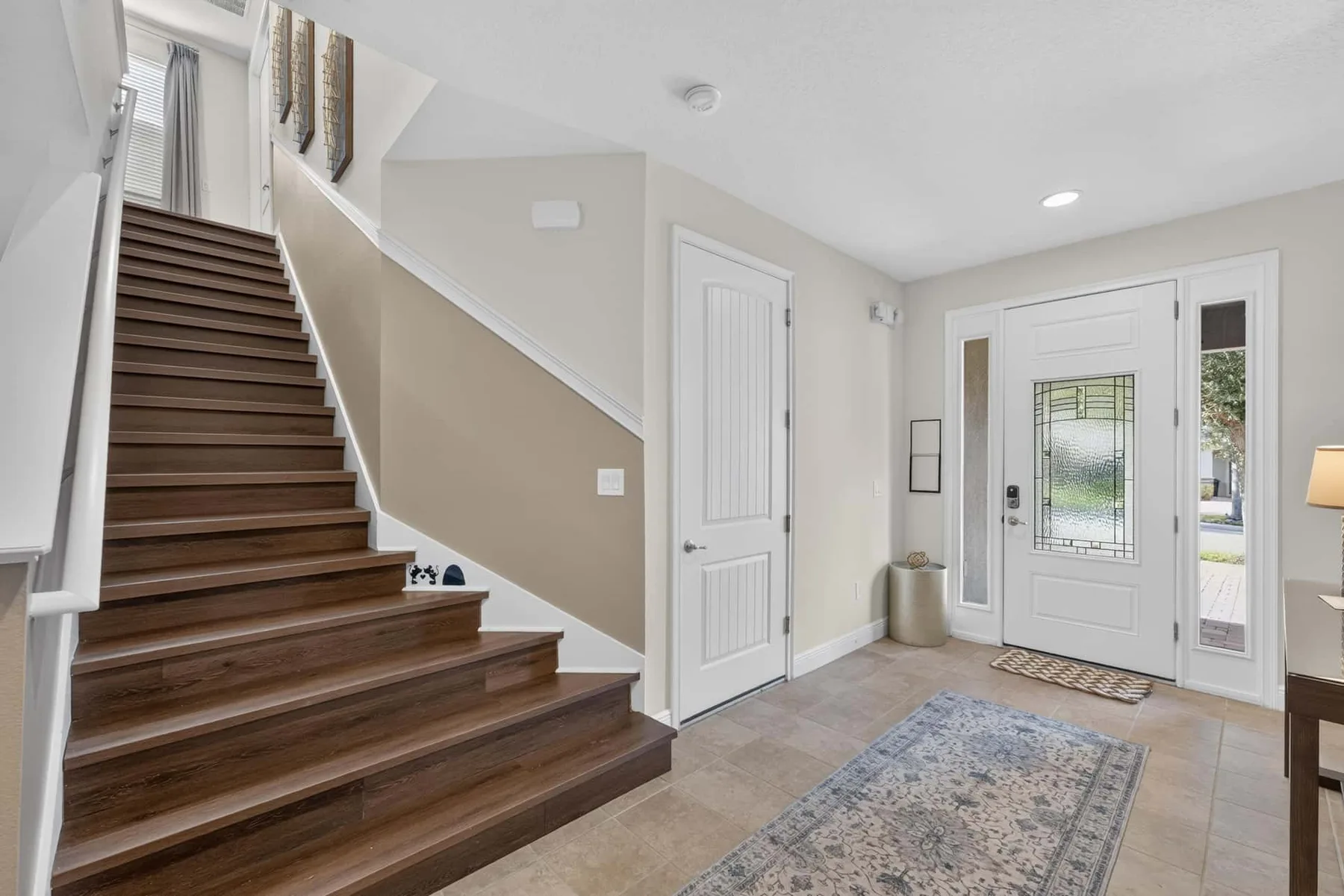 A bright entryway features a wooden staircase and a white front door.