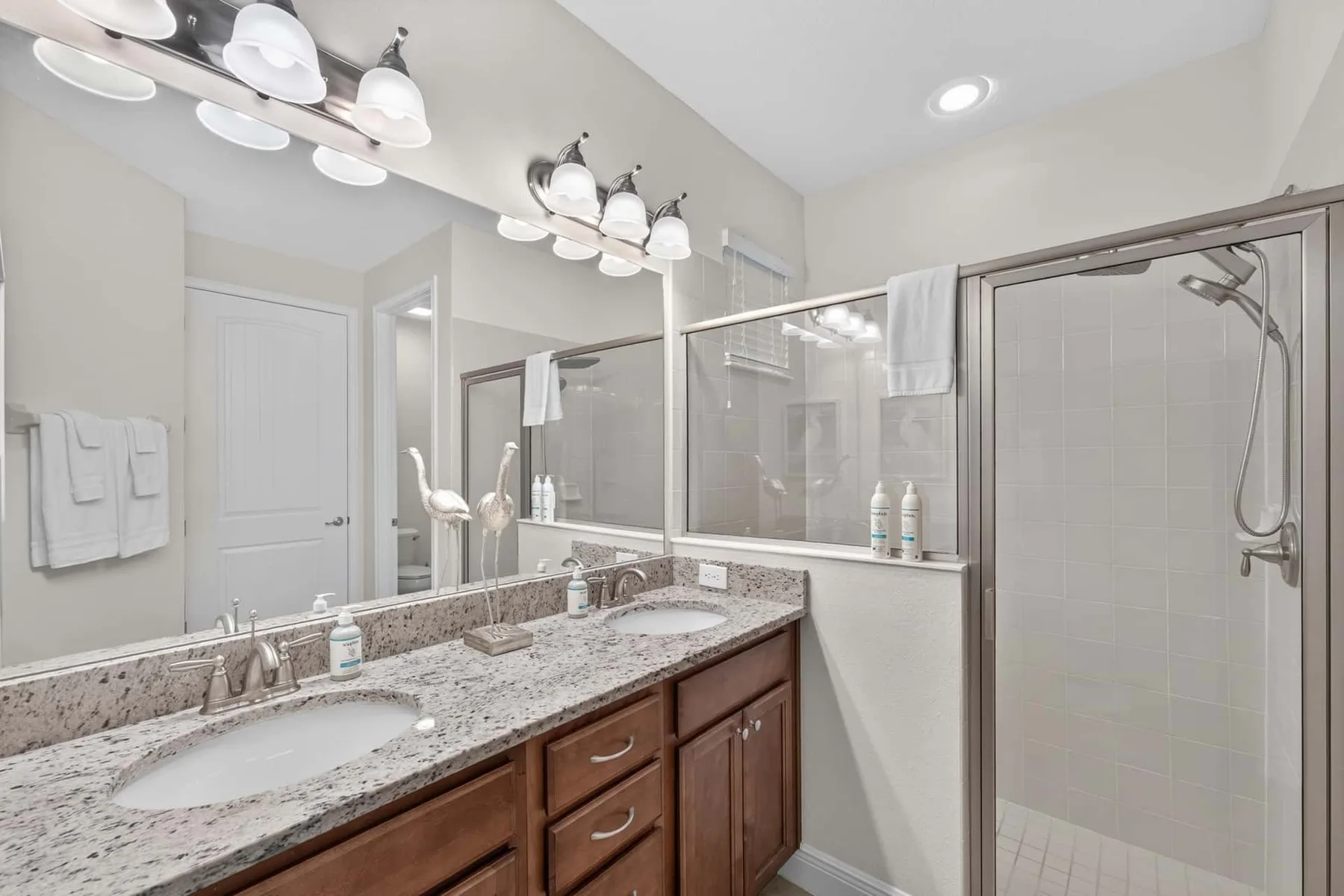 A bright bathroom with a long vanity, two sinks, and a glass shower.