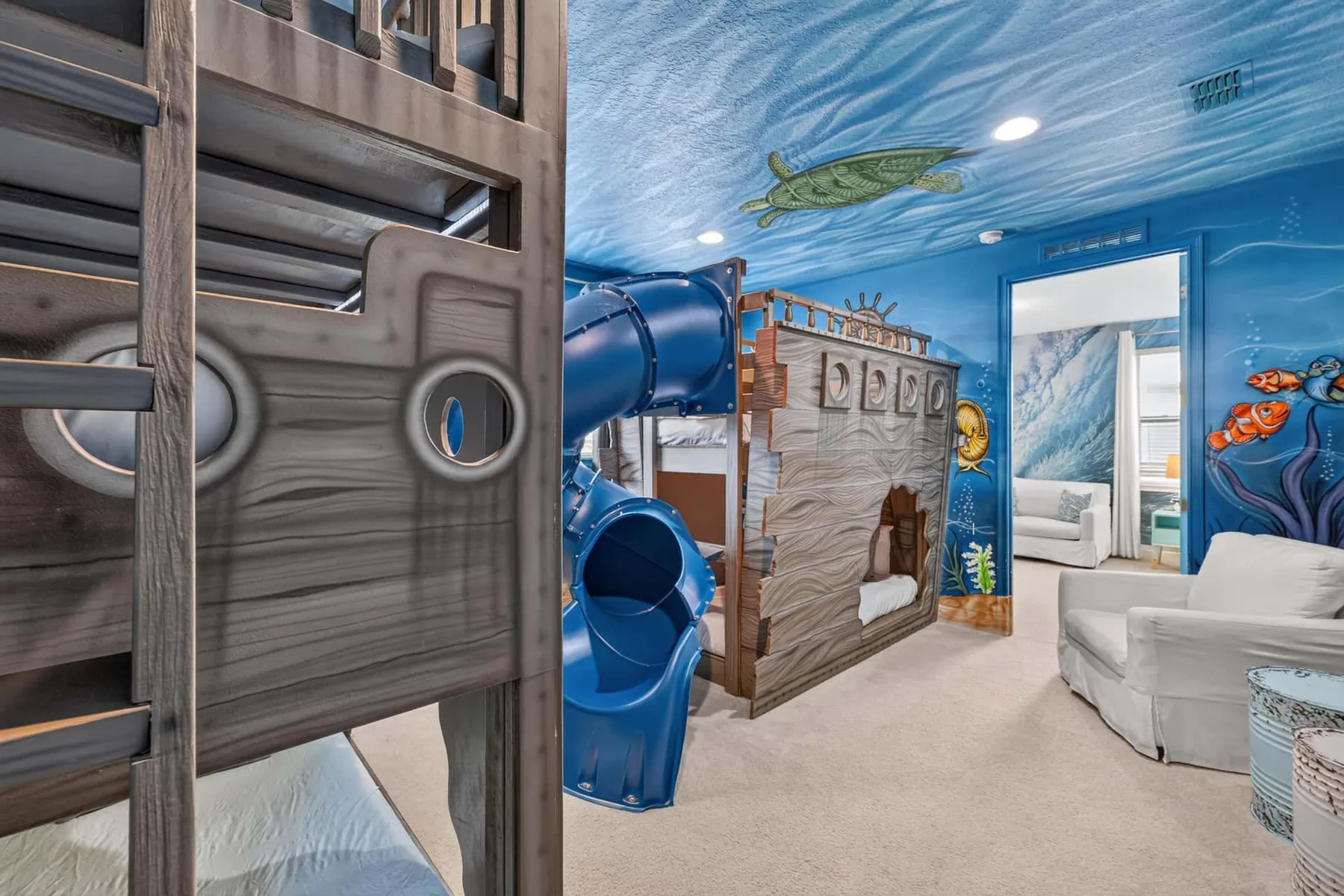 A colorful underwater-themed bedroom features bunk beds, a blue slide, and seating.