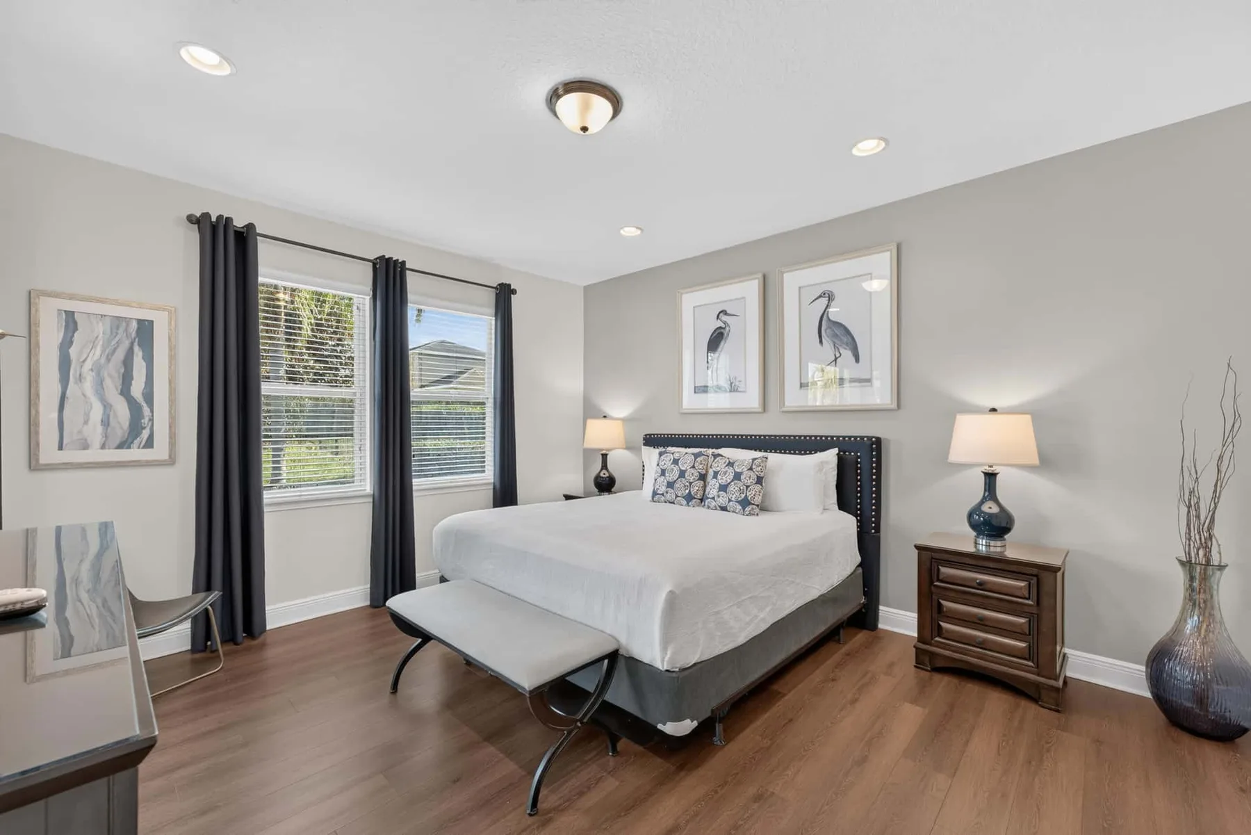 A bedroom with a neatly made bed, framed artwork, and dark curtains.