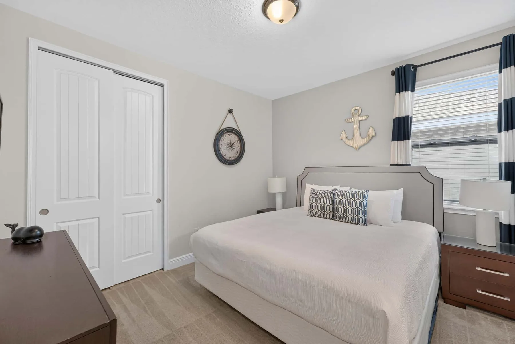 A bedroom with a neatly made bed, bedside tables, and a window with striped curtains.