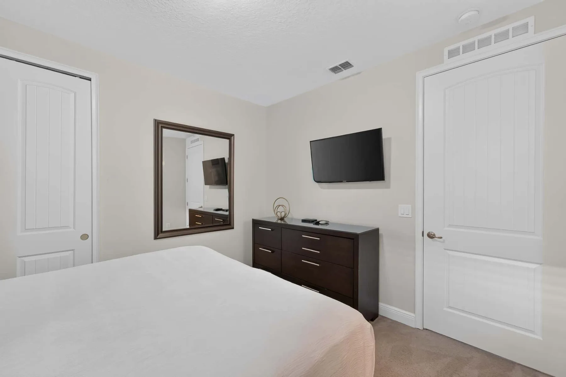 A bedroom with a bed, a wall-mounted television, and a dark dresser.