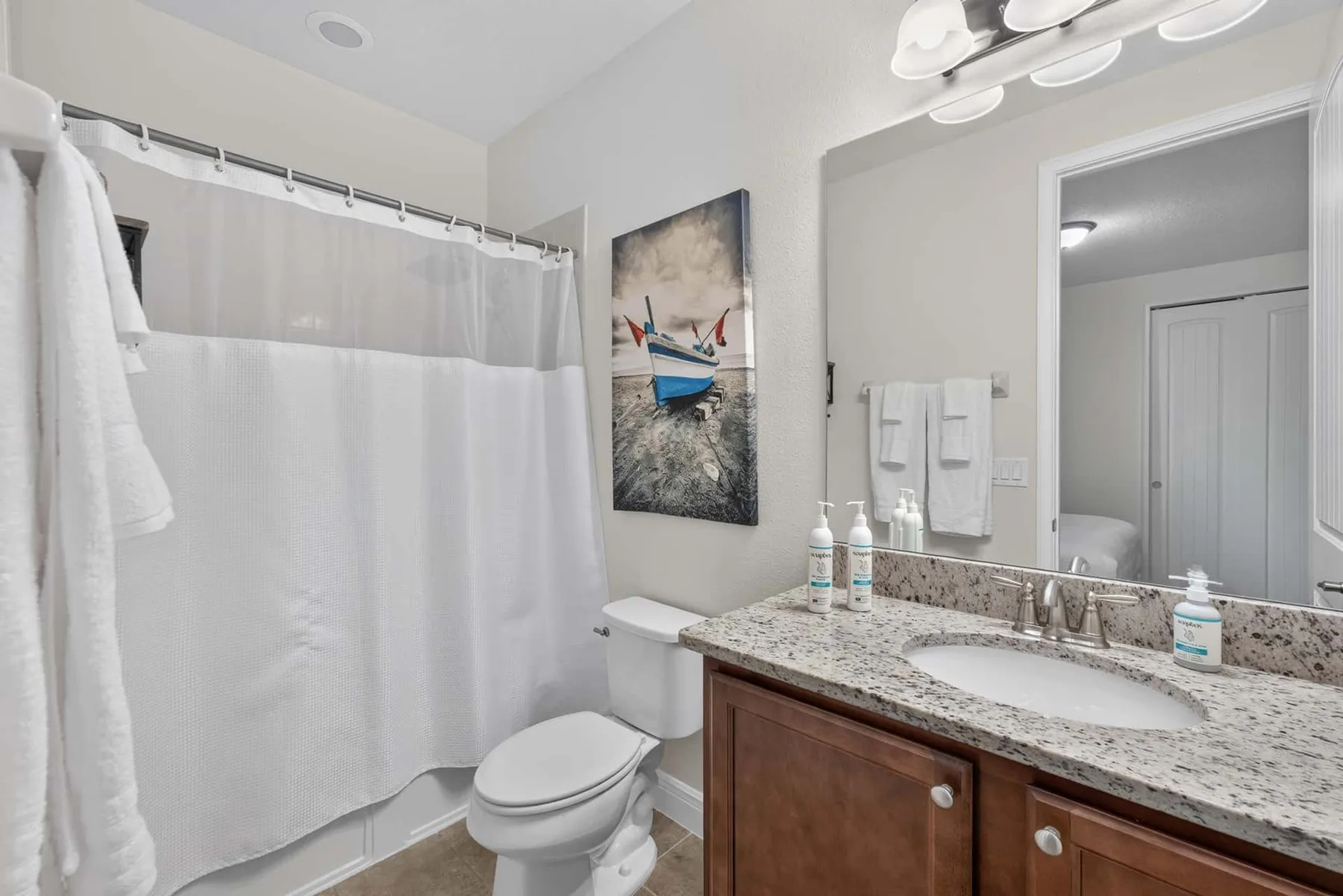 A bathroom with a curtained shower, toilet, and vanity with a large mirror.
