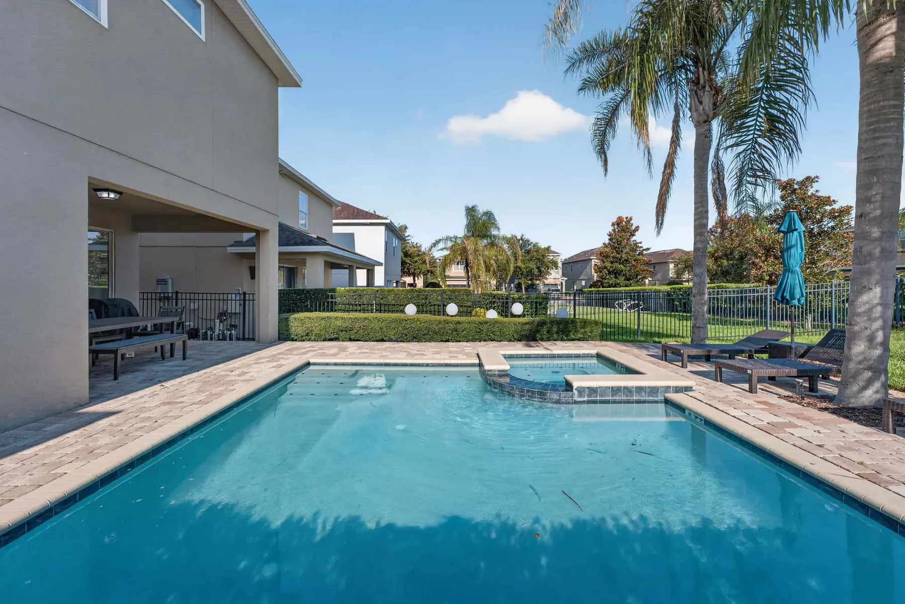 A backyard swimming pool beside a covered patio and palm trees.