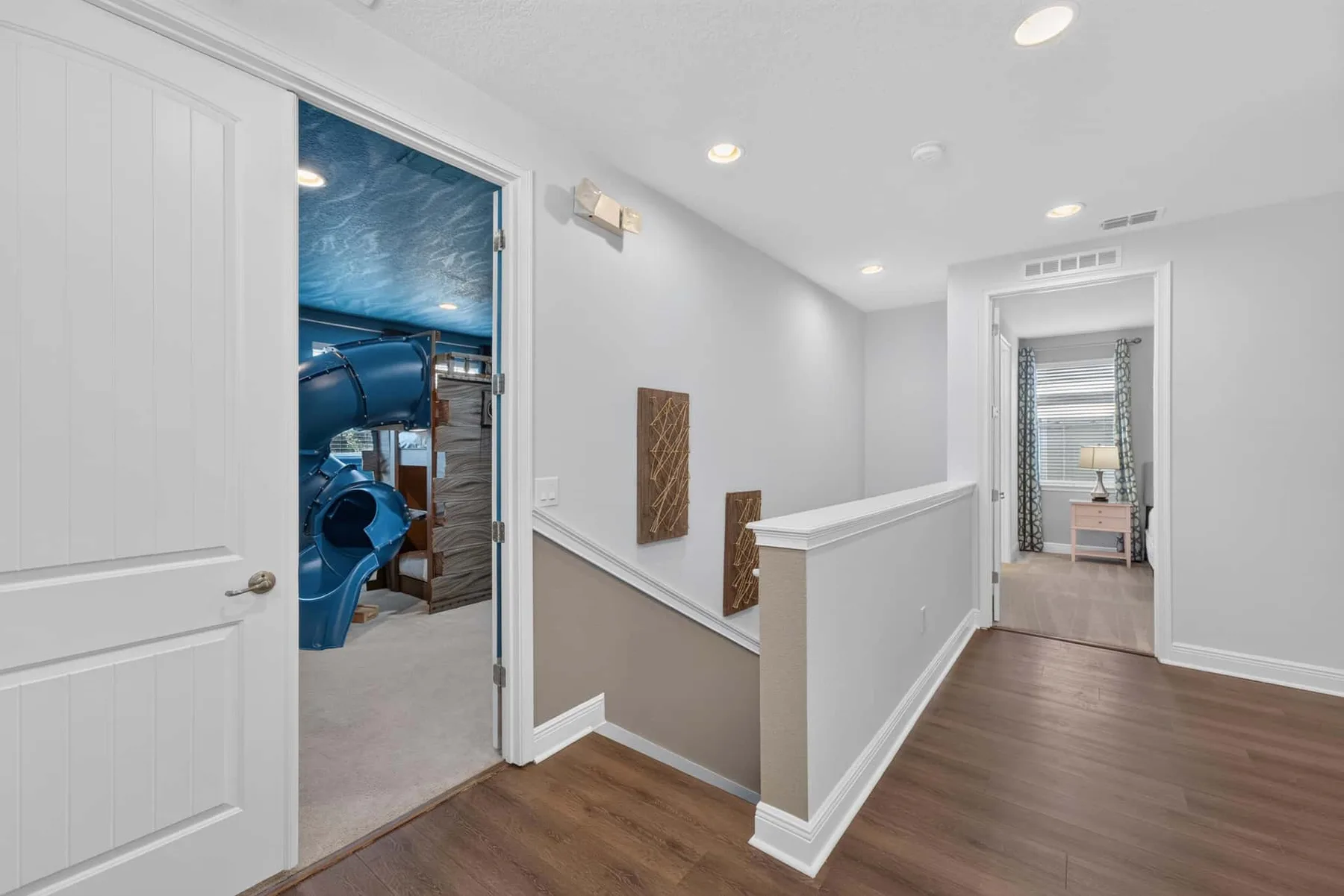 A bright upstairs hallway leads to a room with blue exercise equipment.