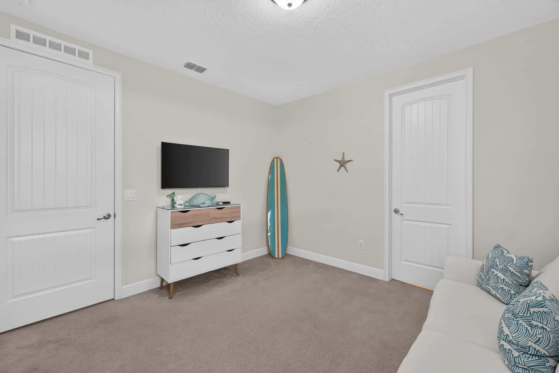 A carpeted bedroom with a dresser, television, surfboard, and seating.