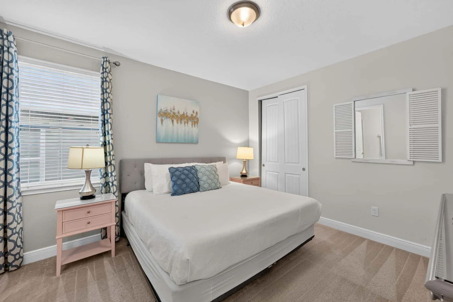A bedroom with a neatly made bed, bedside tables, and a window with patterned curtains.