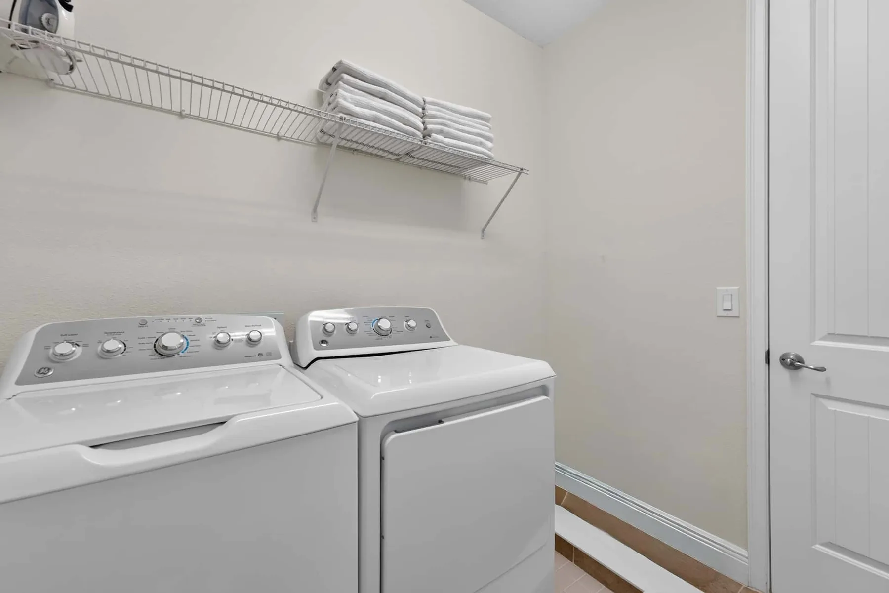 A laundry room with a washer and dryer beneath a wall-mounted shelf.