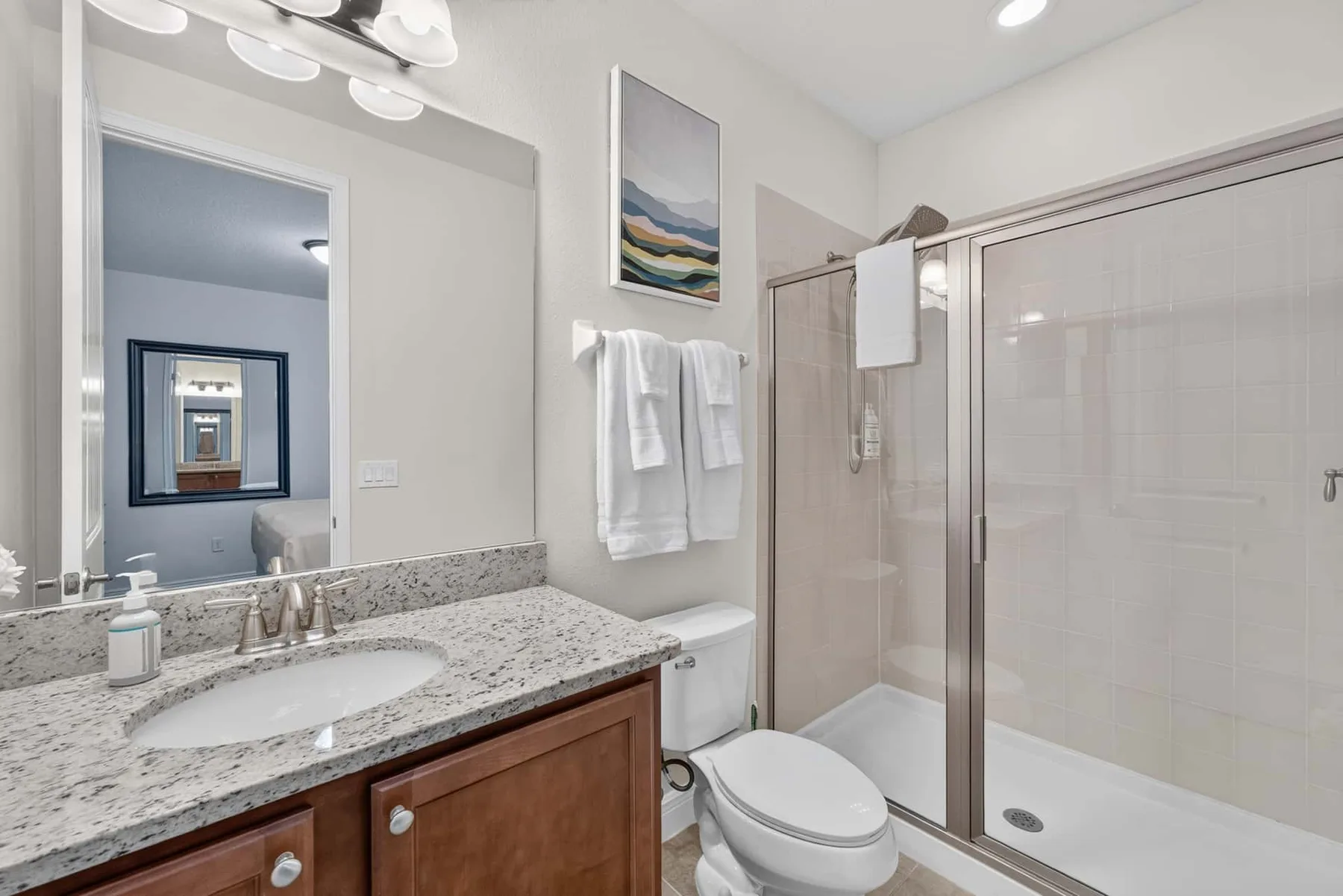 A bathroom with a granite vanity, toilet, and glass shower.