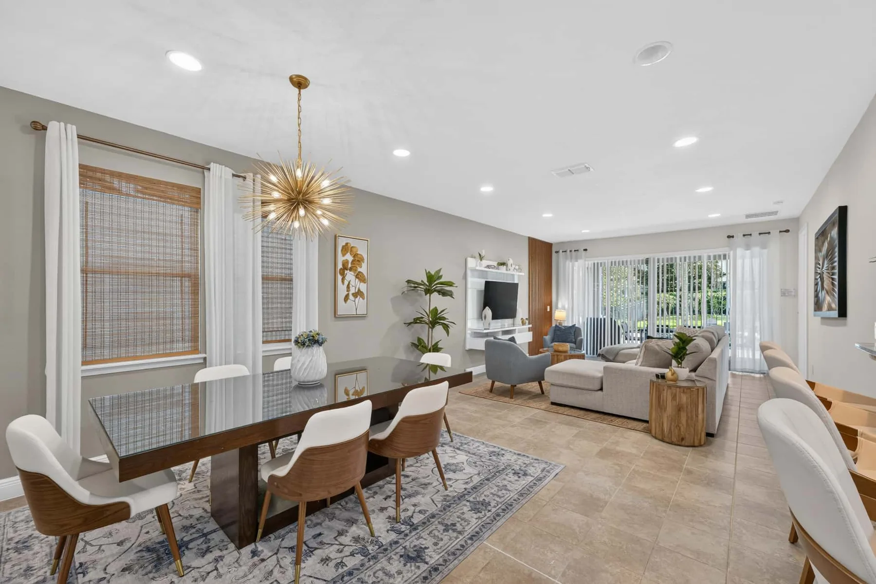 An open dining and living area features a long table and seating by broad windows.