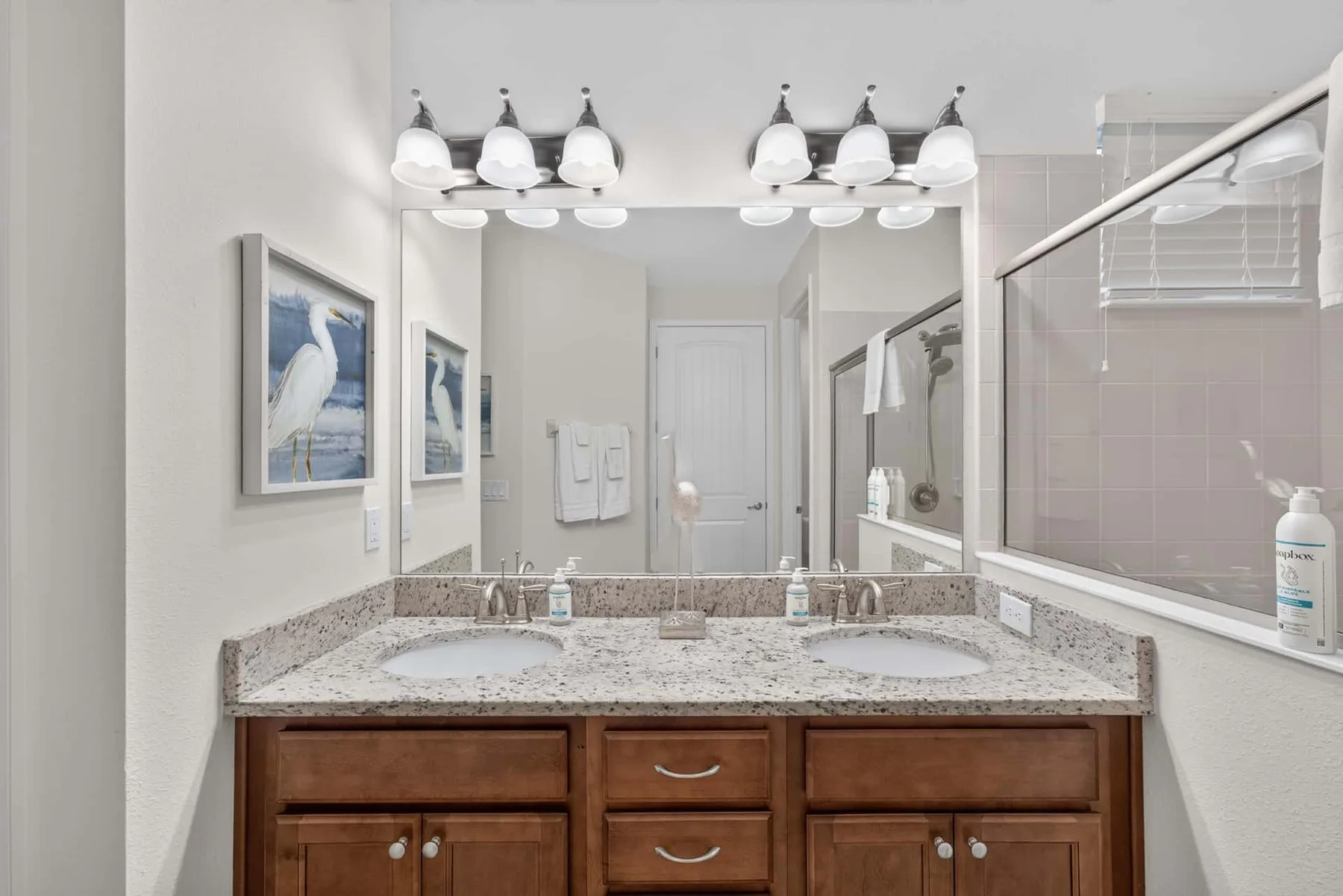 A bathroom vanity with a wide mirror and framed wall art.