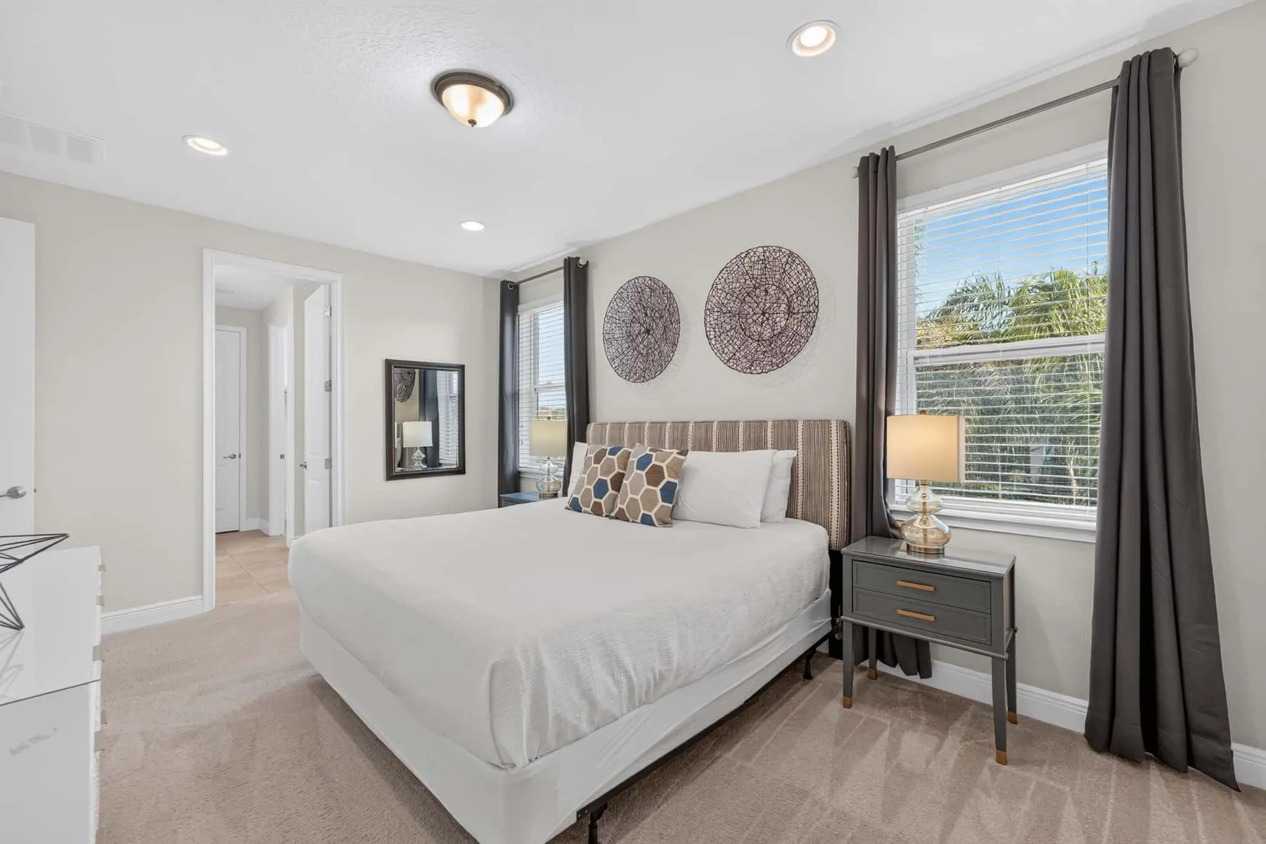A bright bedroom with a neatly made bed and windows with dark curtains.