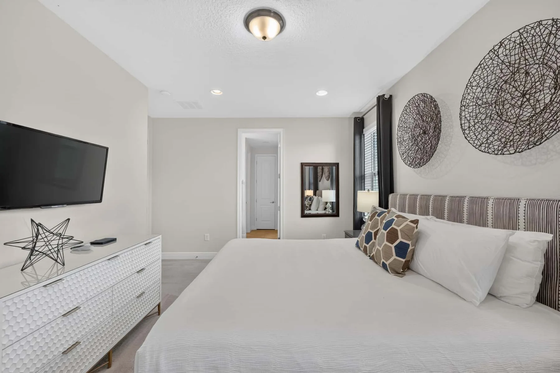 A bright bedroom with a neatly made bed and a television mounted on the wall.