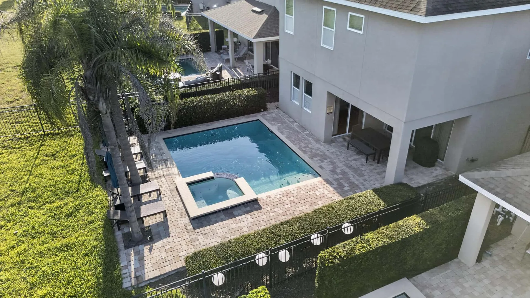 An aerial view of a backyard pool beside a two-story house and patio.