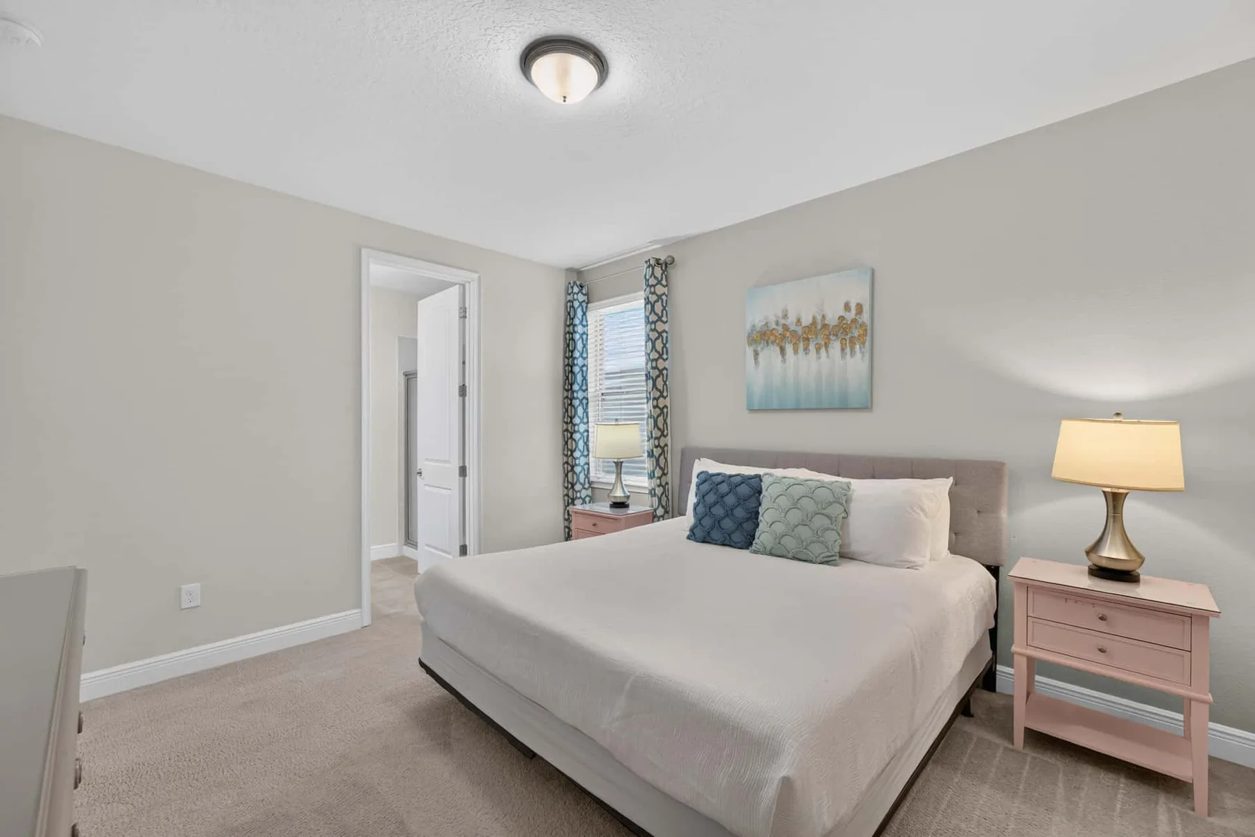 A bedroom with a neatly made bed, bedside table, and window.