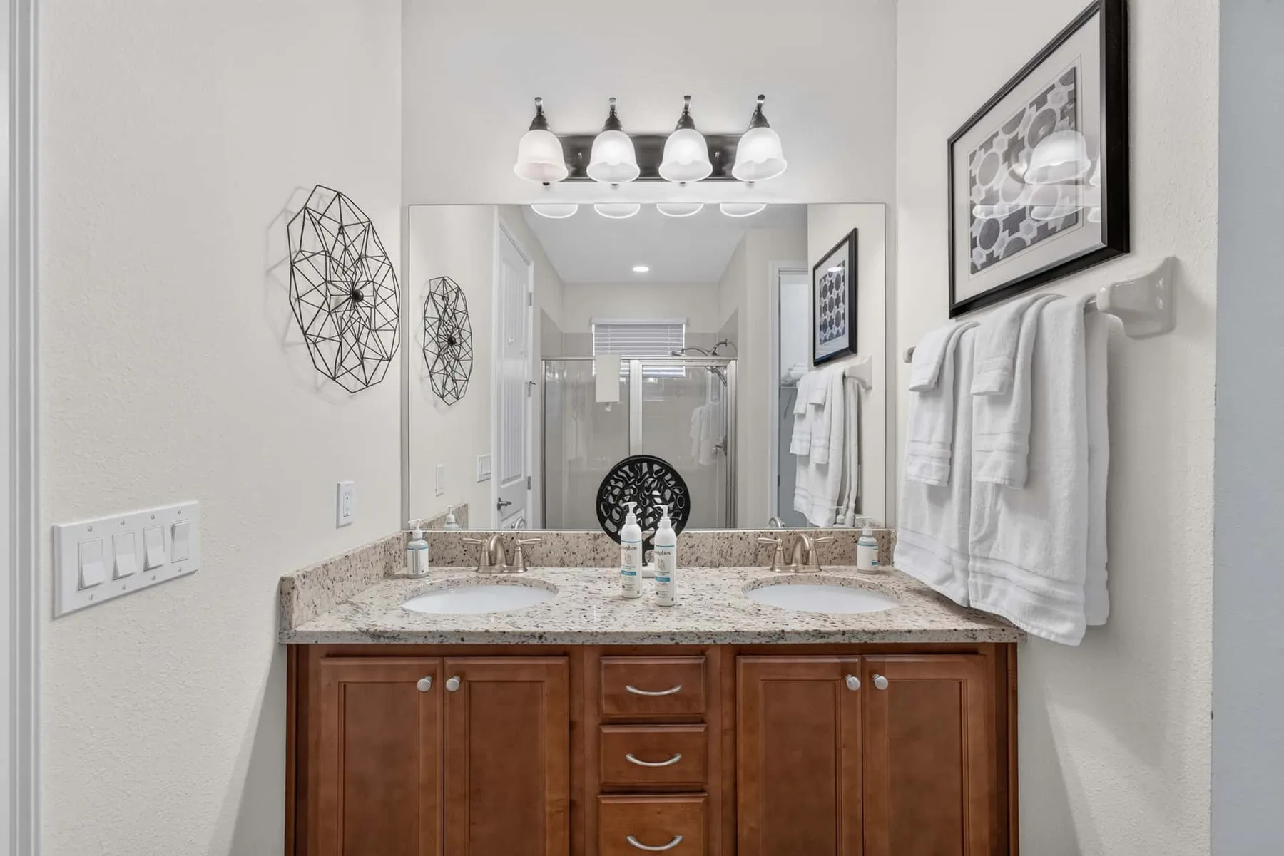 A bathroom vanity with a wide mirror, twin sinks, and wall-mounted towels.