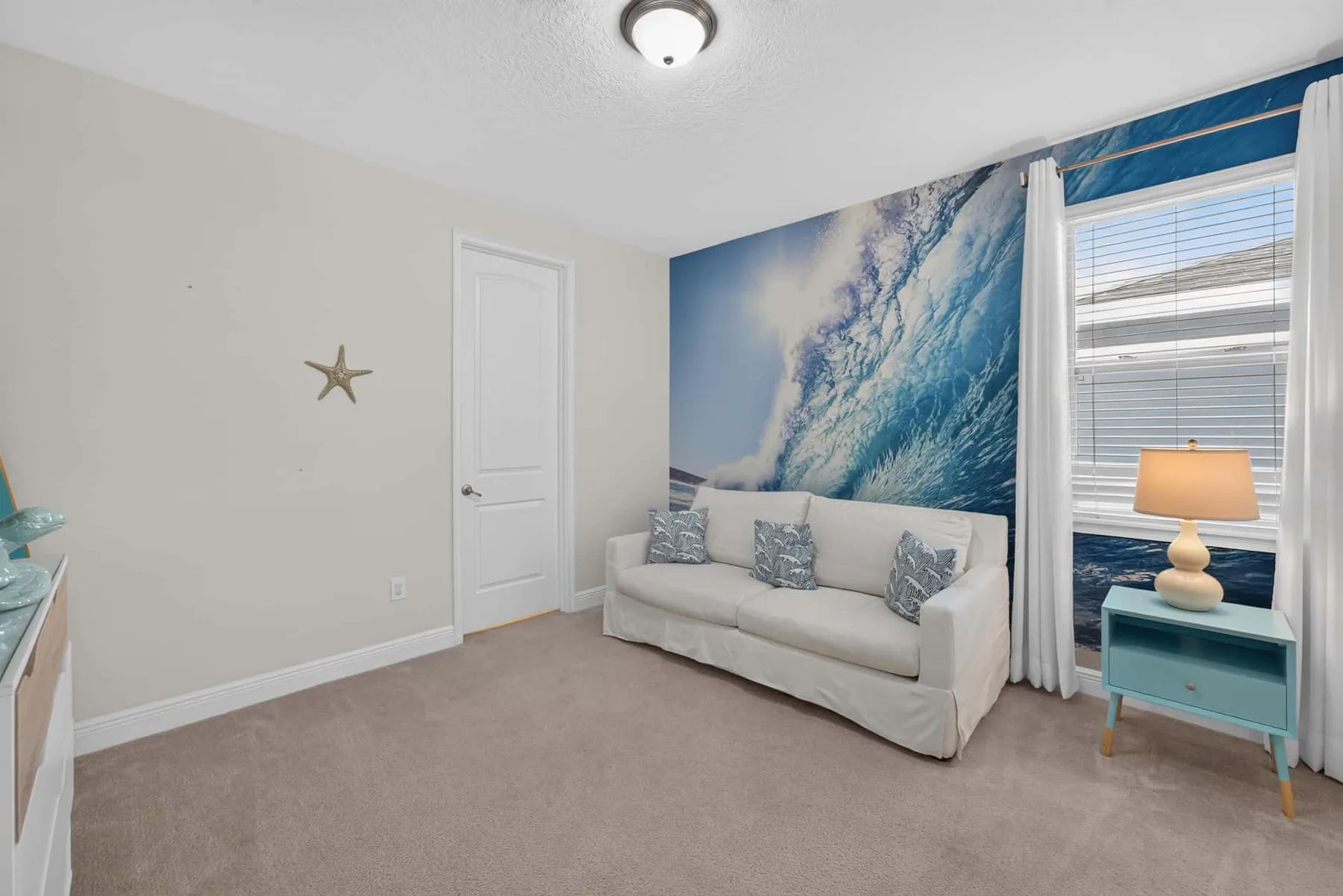 A living room with a light sofa beneath a large ocean-wave wall mural.