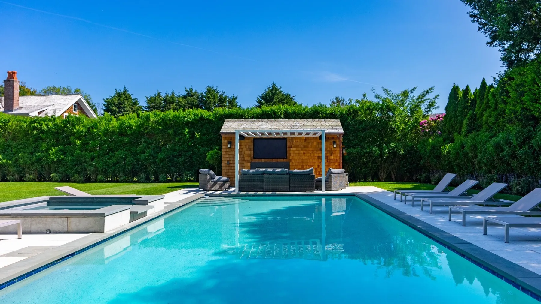 An outdoor swimming pool with a small wooden poolside structure and lounge chairs.