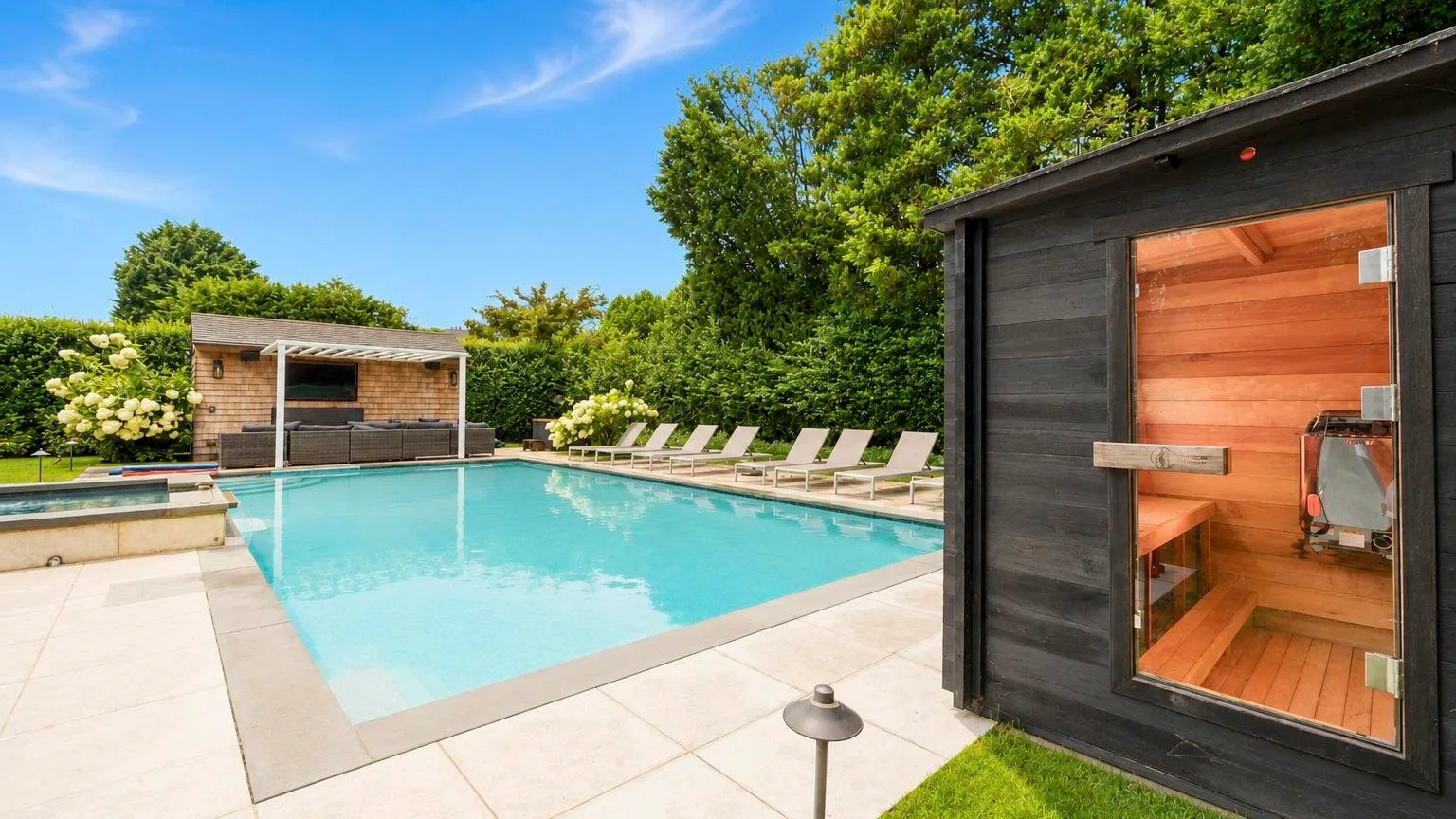 An outdoor swimming pool beside a wooden sauna and lounge chairs.