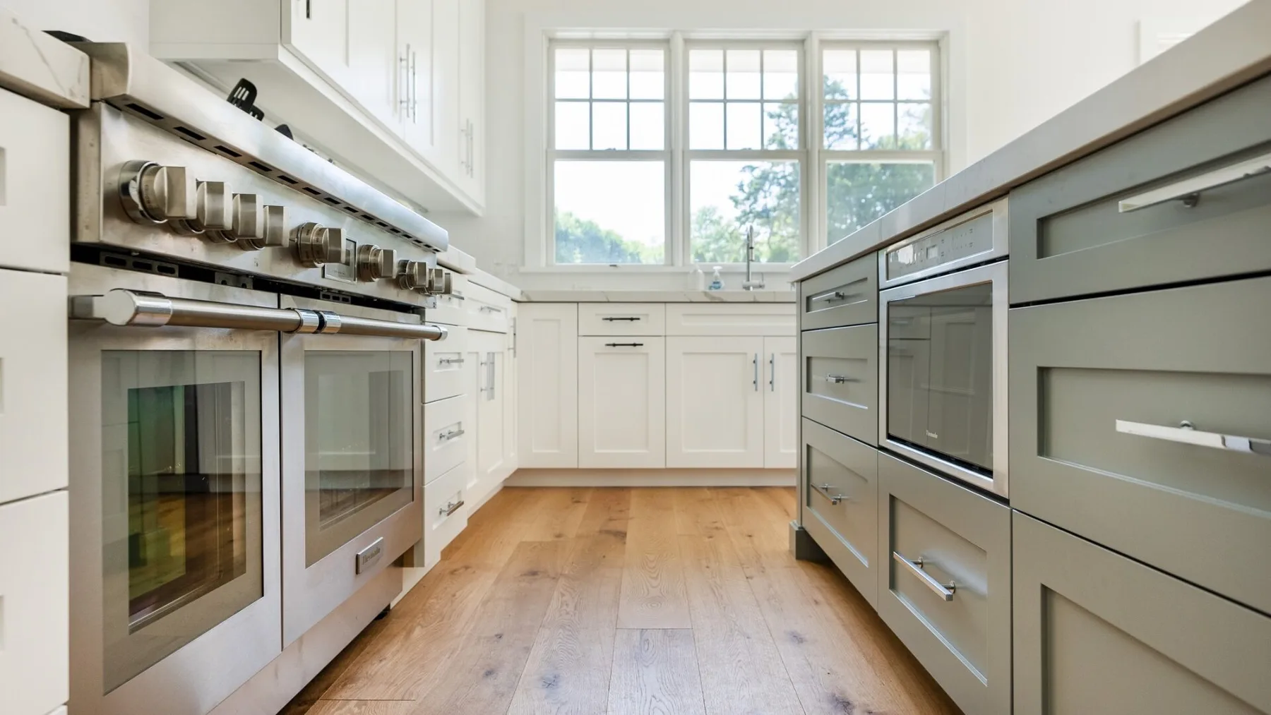 A bright kitchen with white cabinetry, stainless steel appliances, and large windows.