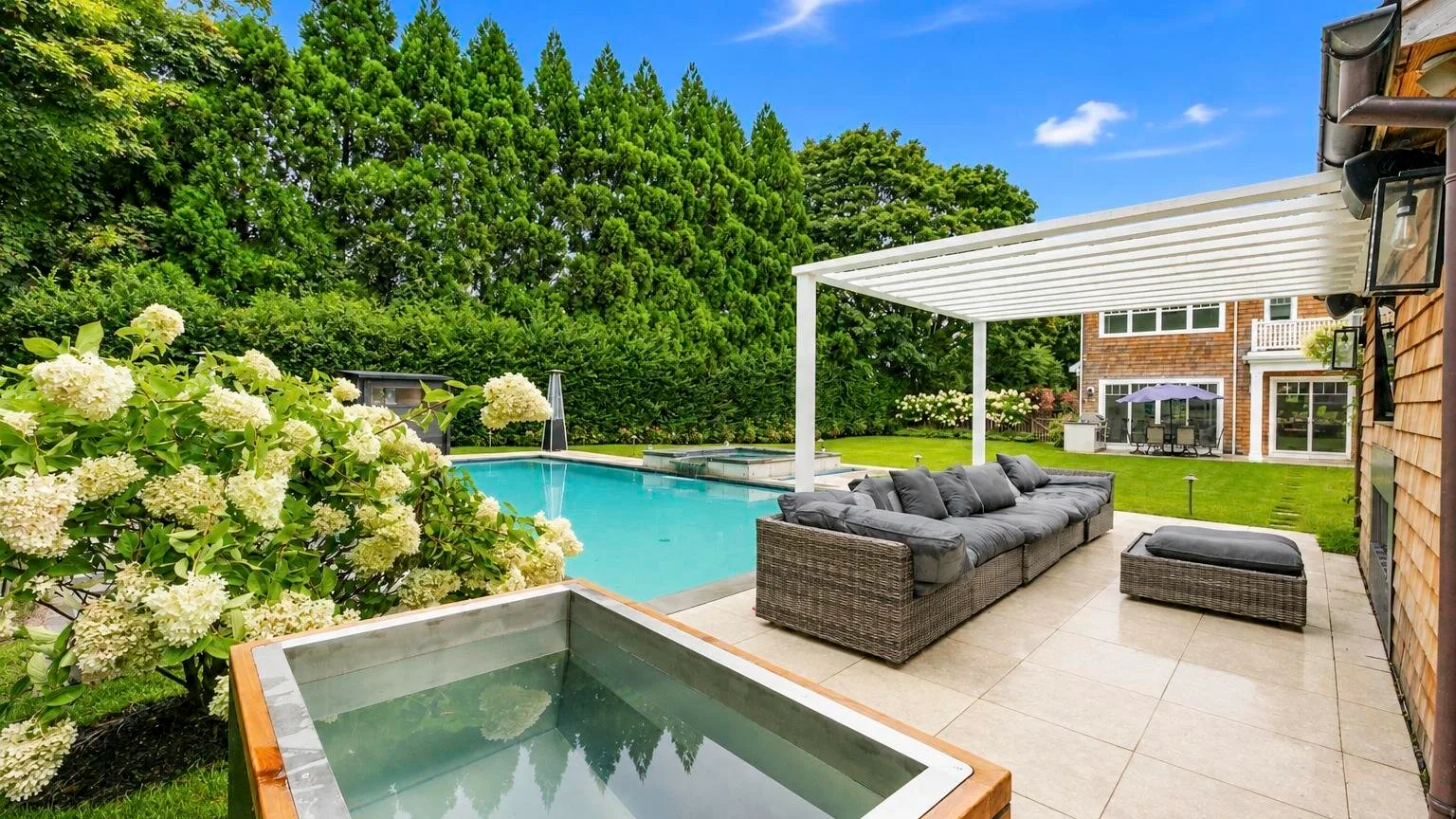 A backyard patio with a swimming pool, hot tub, and outdoor seating beneath a pergola.